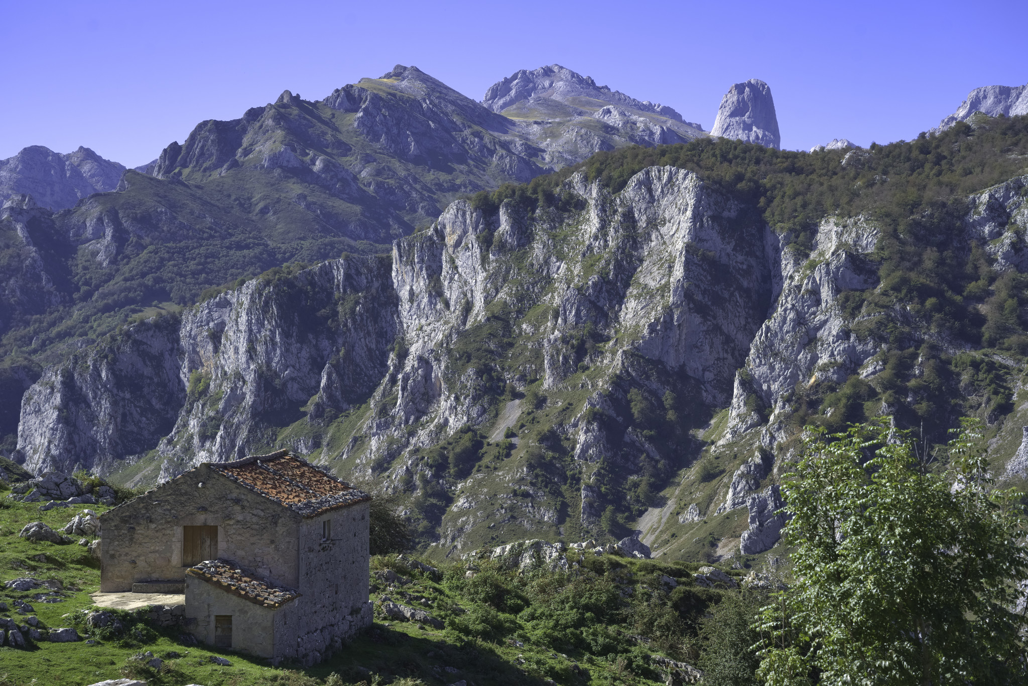 A small house sits on a plateau with distant views to high peaks