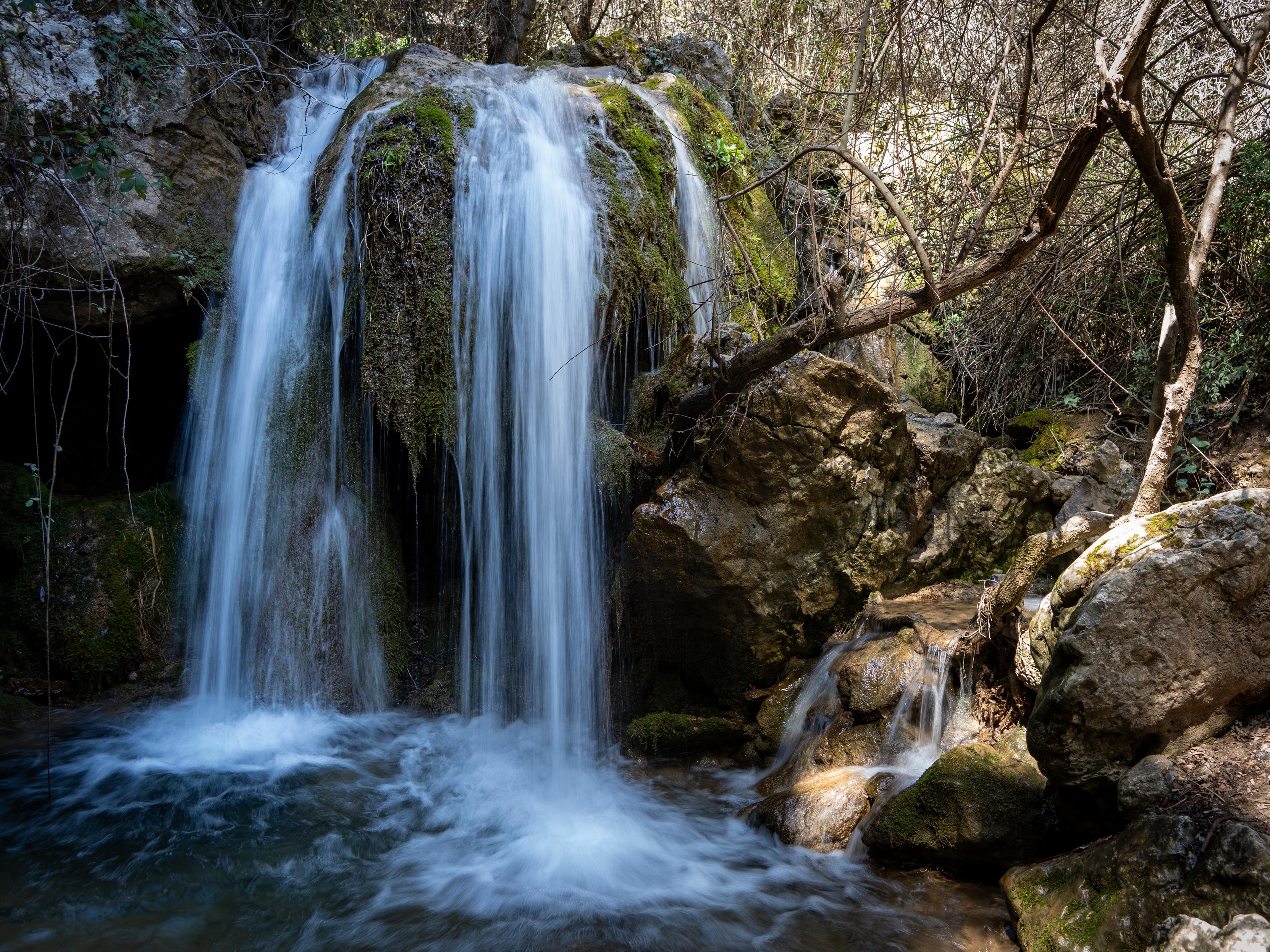 A waterfall is plunging over a series of falls whilst a small stream enters from the right over colorful rocks and boulders