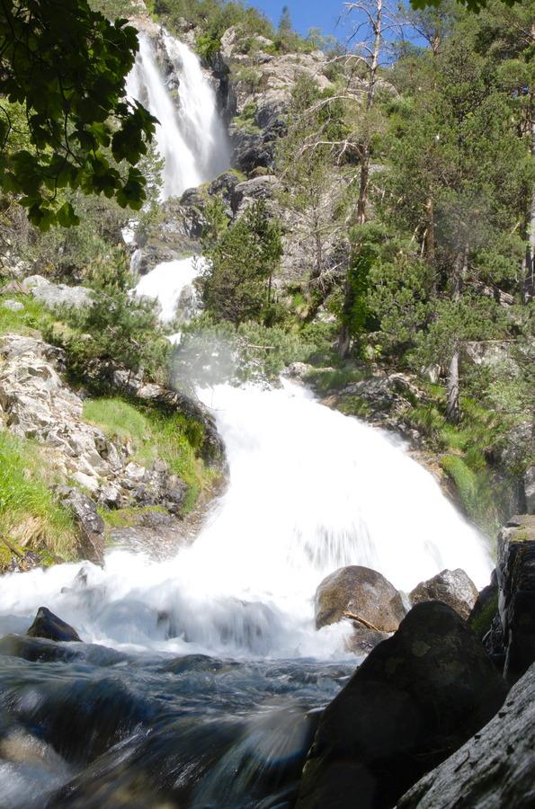A huge waterfall comes down the mountainside surrounded on both sides by forest and lush vegetation