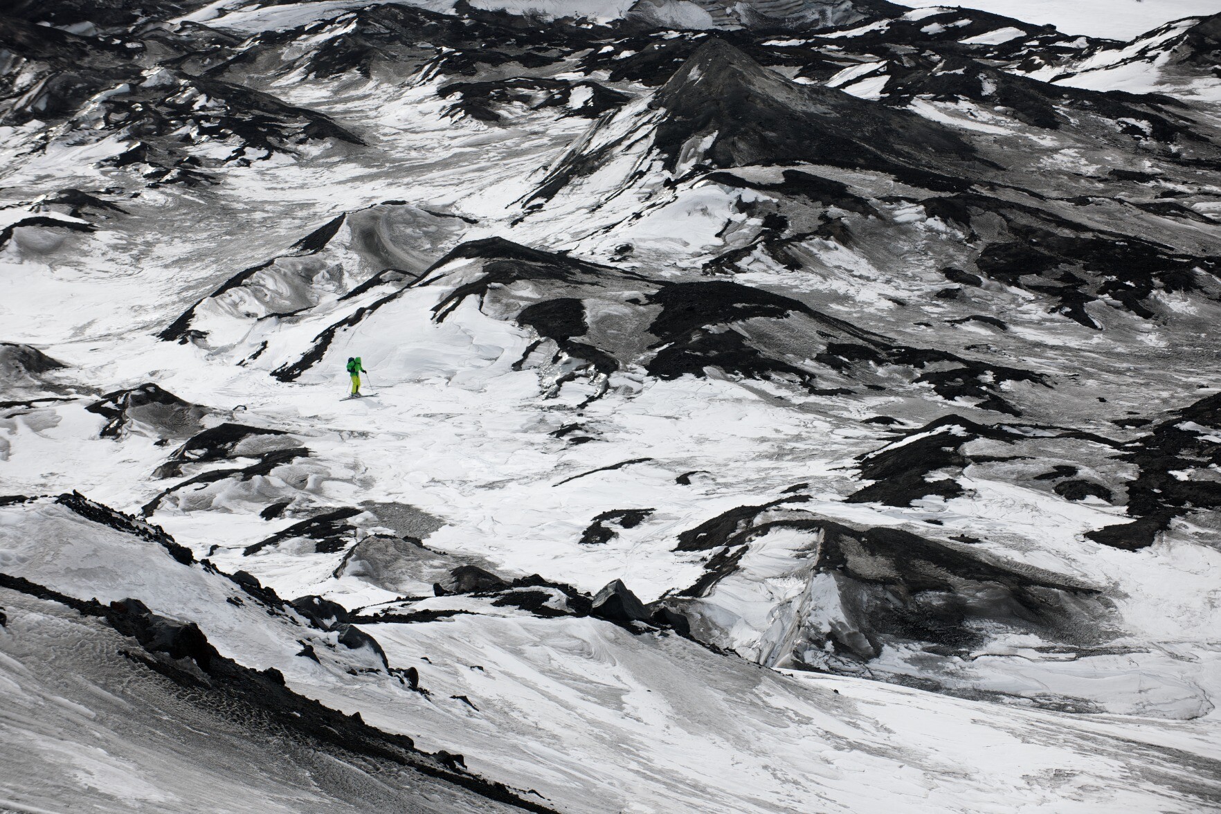 A lone skier negotiating the rocky and volcanic dust laden glacier.