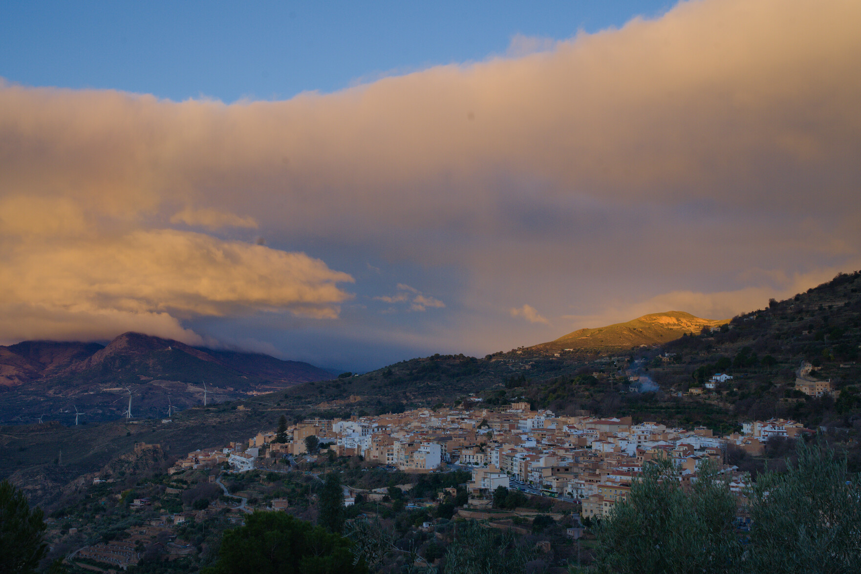 Shows a spanish town with morning sunrise arriving. Clouds above town