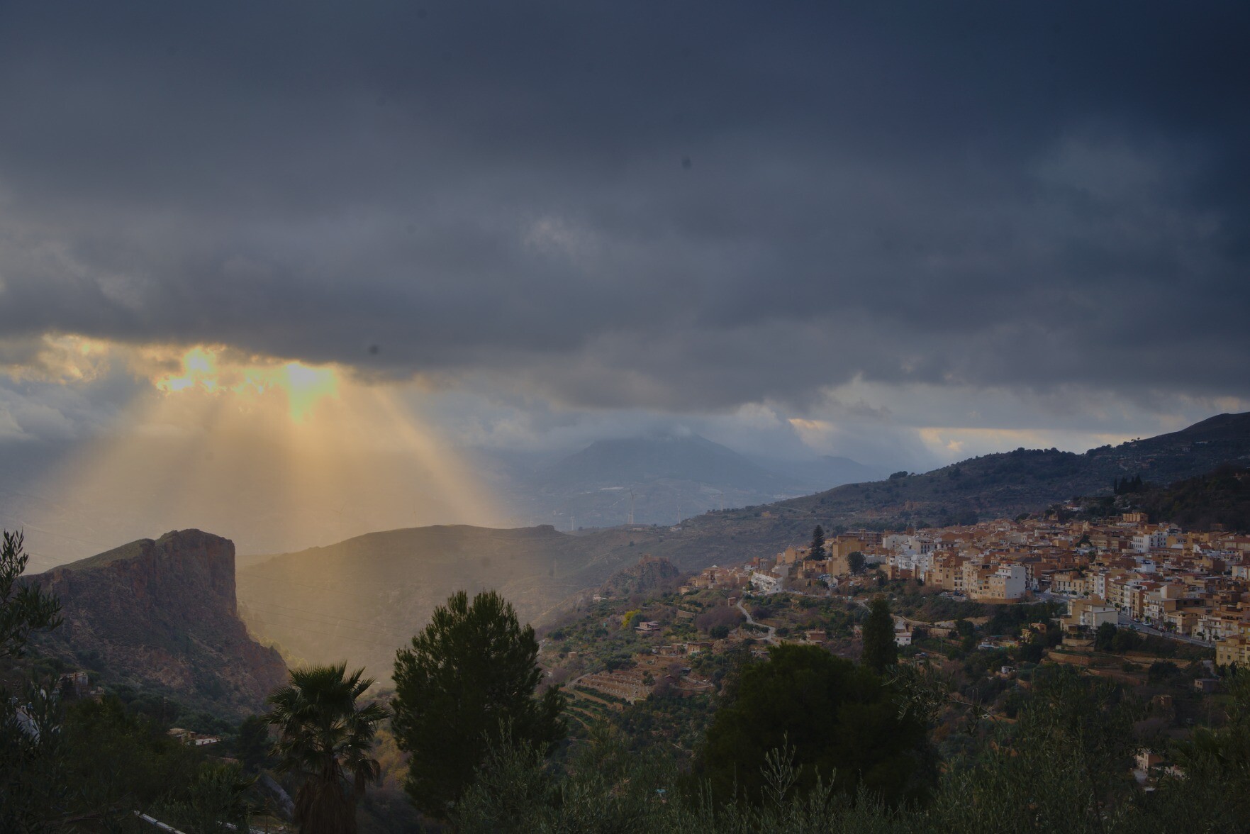 Beautiful evening light coming through the clouds over some cliffs. To the right the spanish town of Lanjaron in the Alpujarras