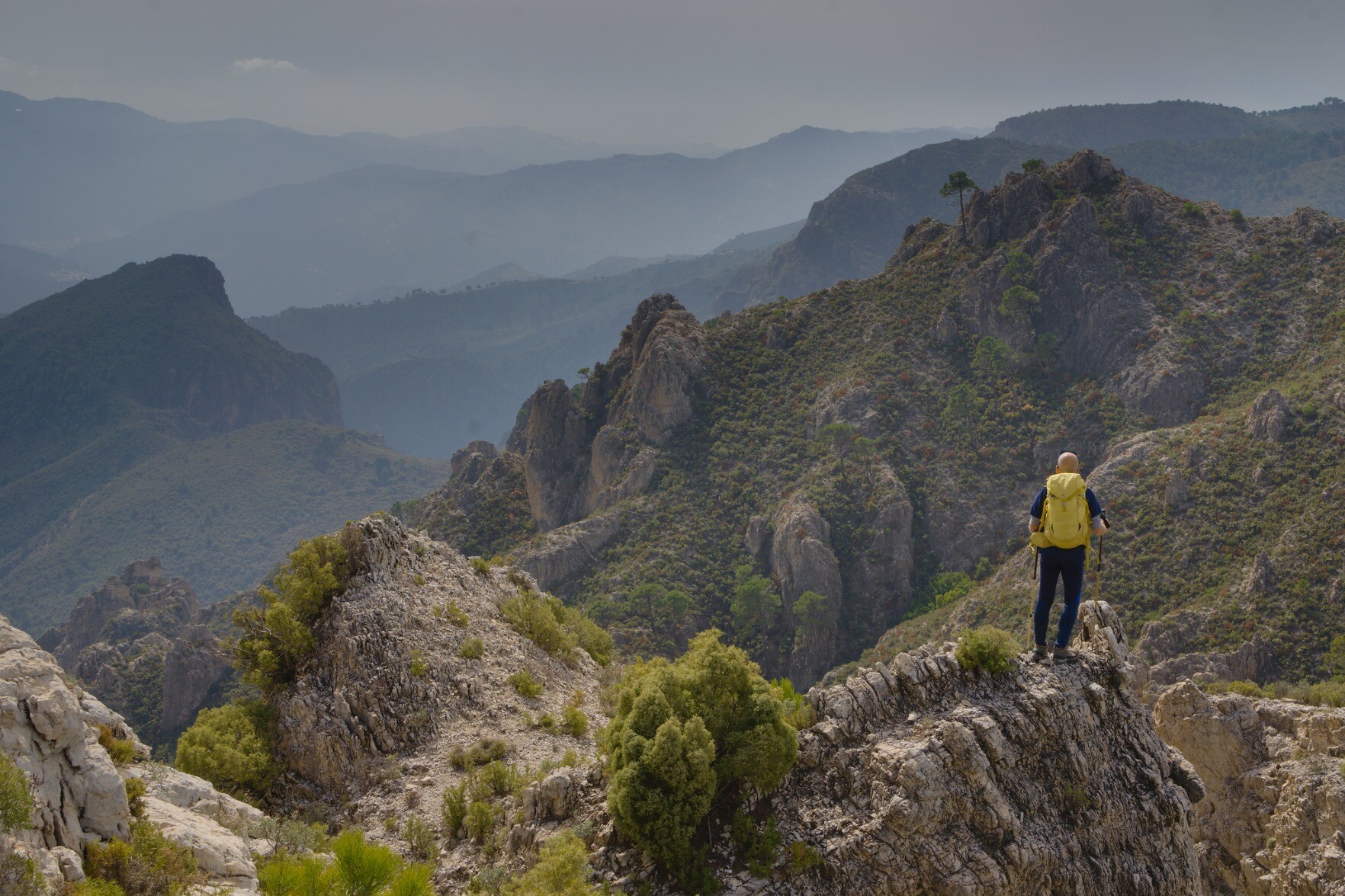 Man stood on a rocky promontory with deep green valleys and high rocky peaks behind. Spain