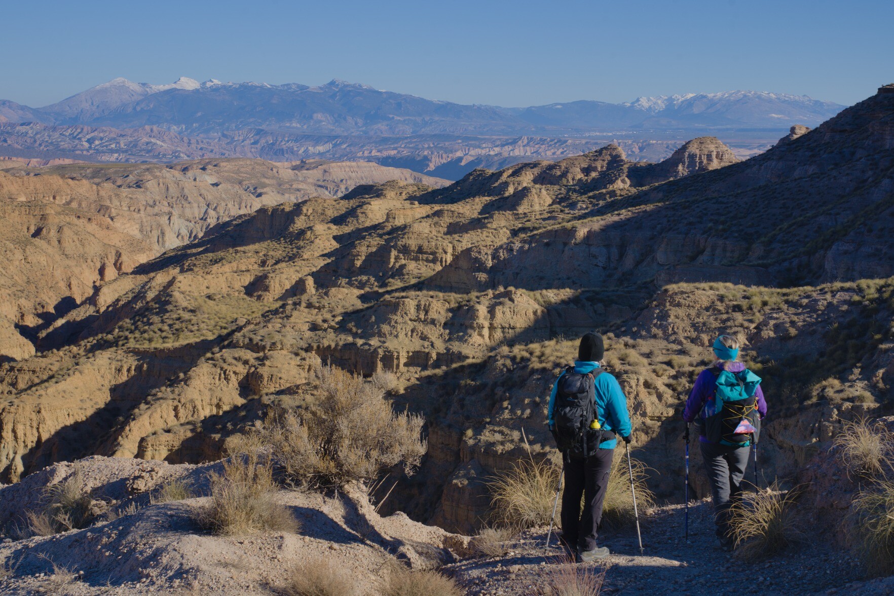 Two hikers stood looking down into a dry desert badlands landscape in southern Spain