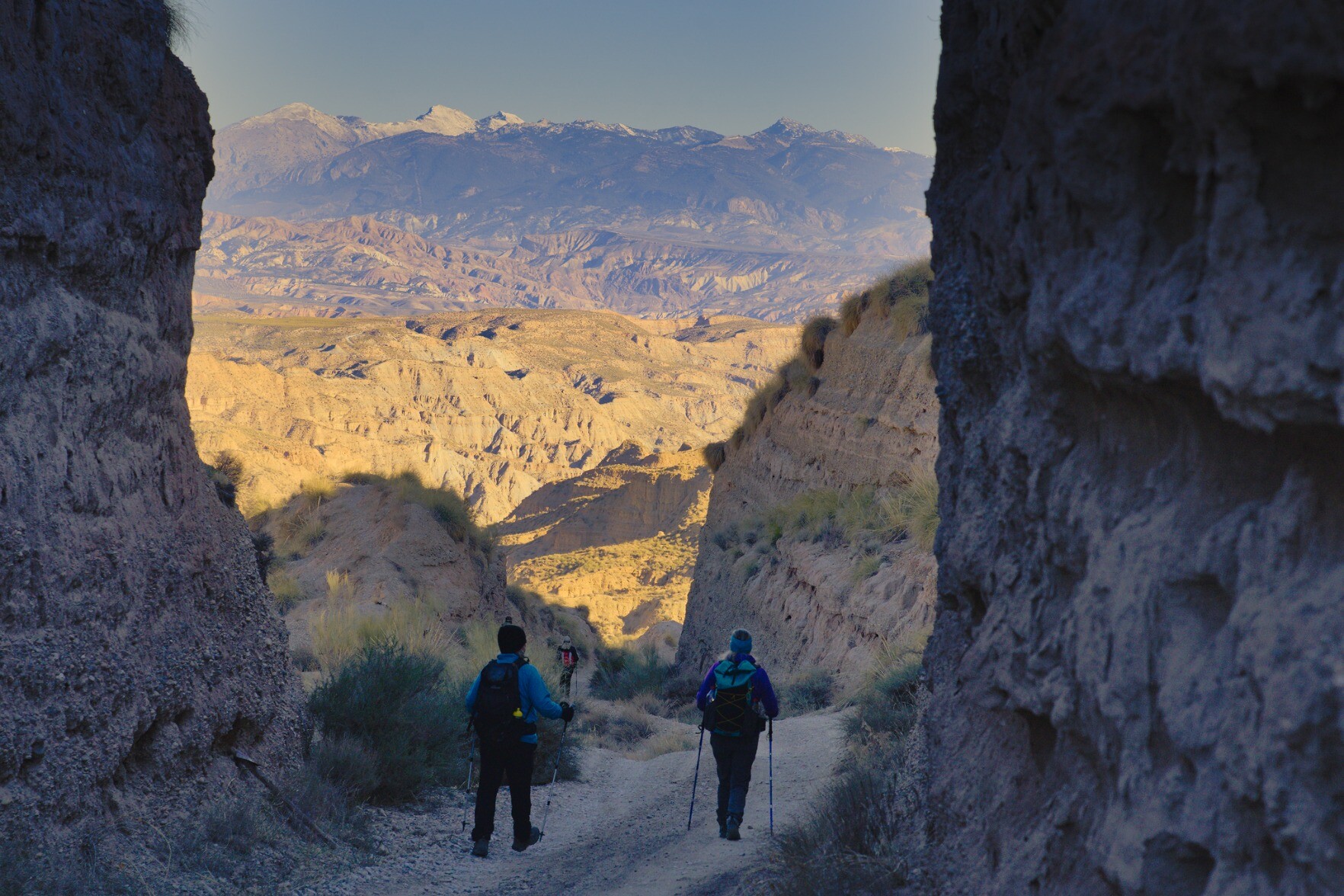 Hikers going through a rock cutting with now capped mountains beyond