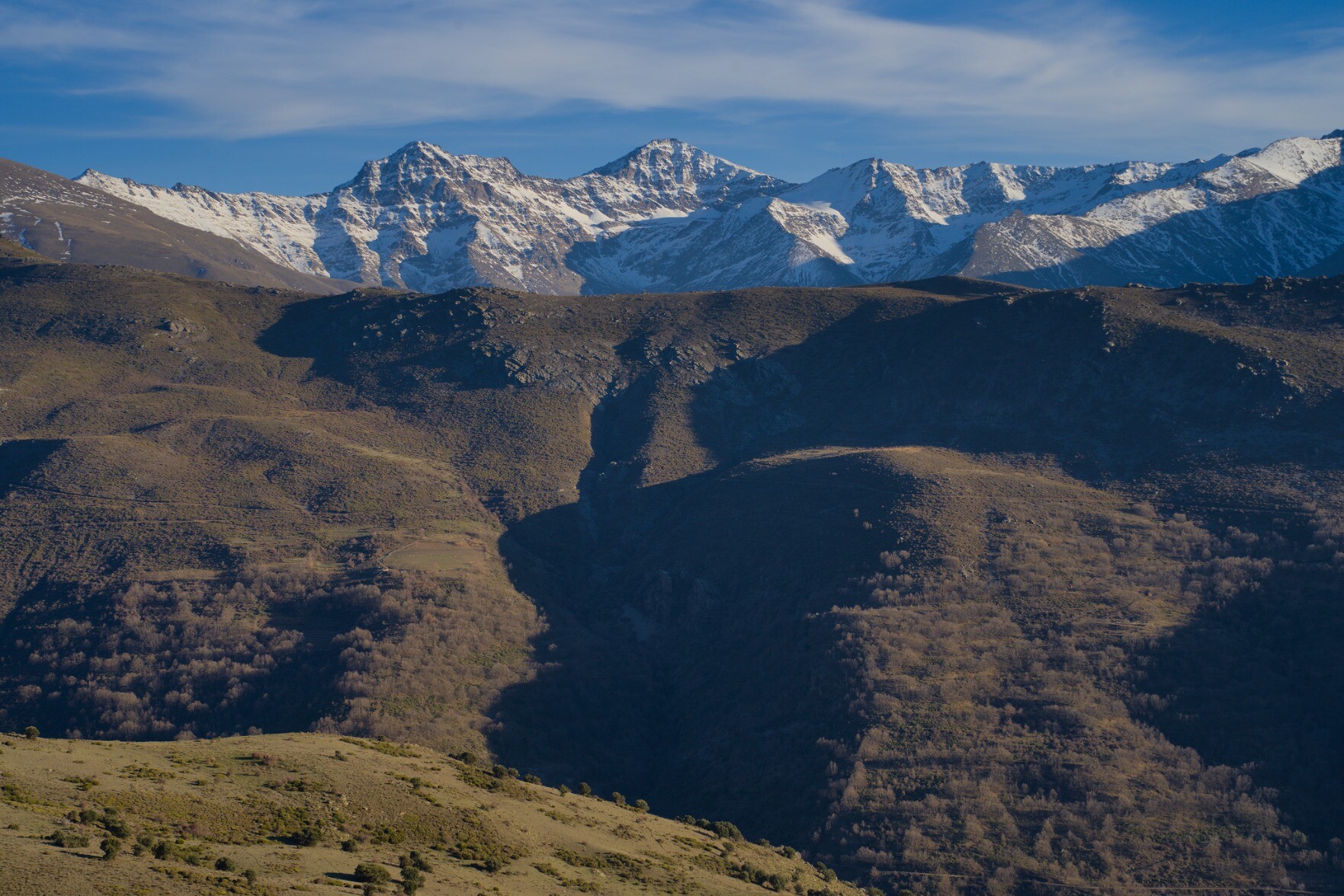 Low winter sun colours on a mountainside with snow clad mountains at the back