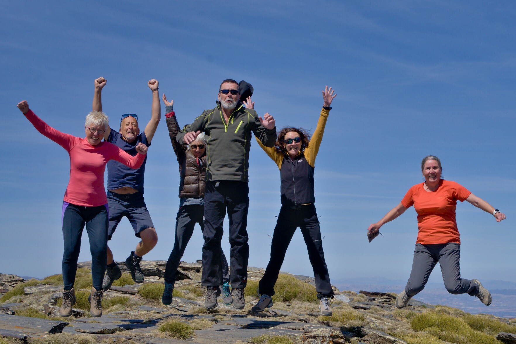 A group of 6 people jumping for joy at being in the high mountains