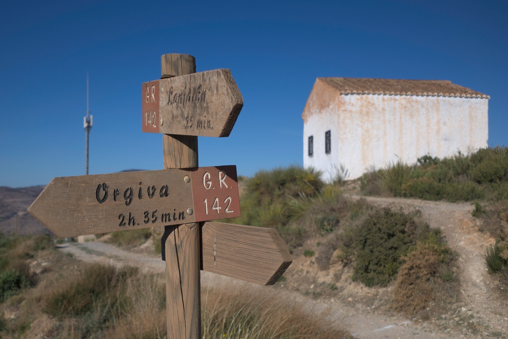 An old trail signpost in the foreground with an old building at the back and to the right