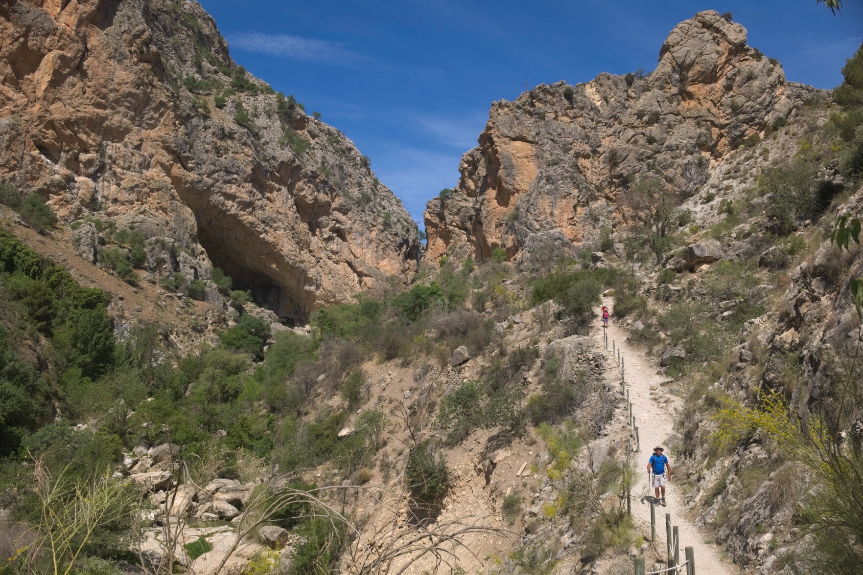 A steep sided rocky valley is to the left. Coming down from the right is a narrow hiking path with some hikers
