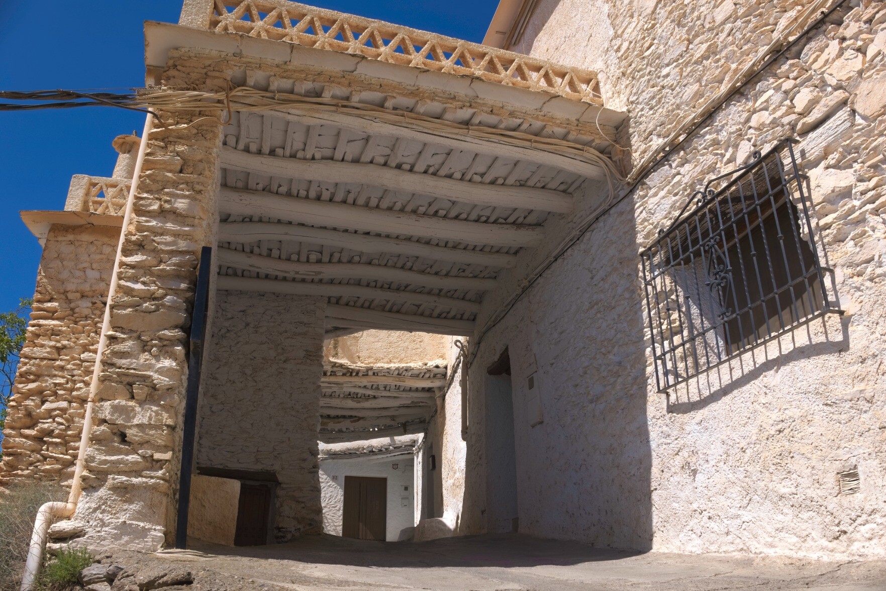 A tunnel through a street. The houses are brown white color and the roof of the tunnel is built with traditional materials.