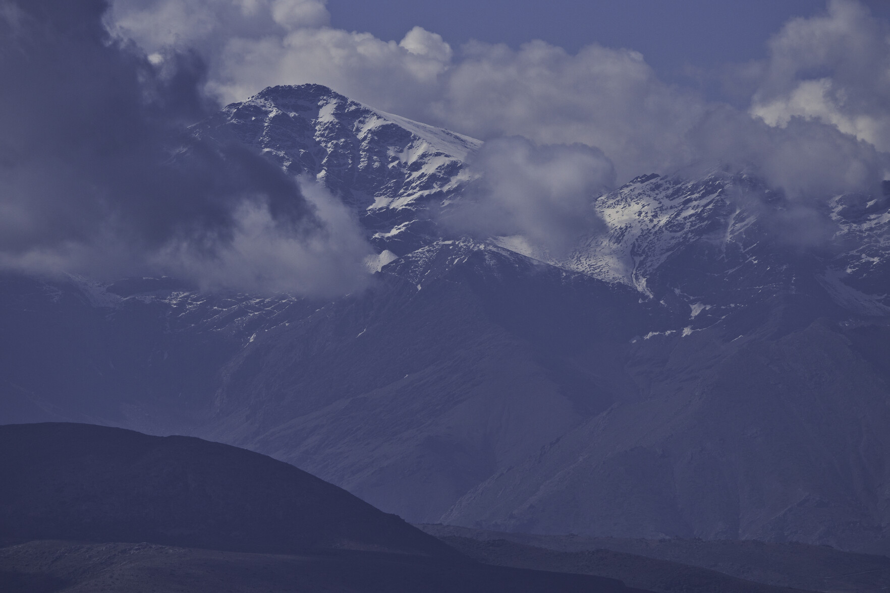 A mountain summit in snow emerges from the surrounding clouds
