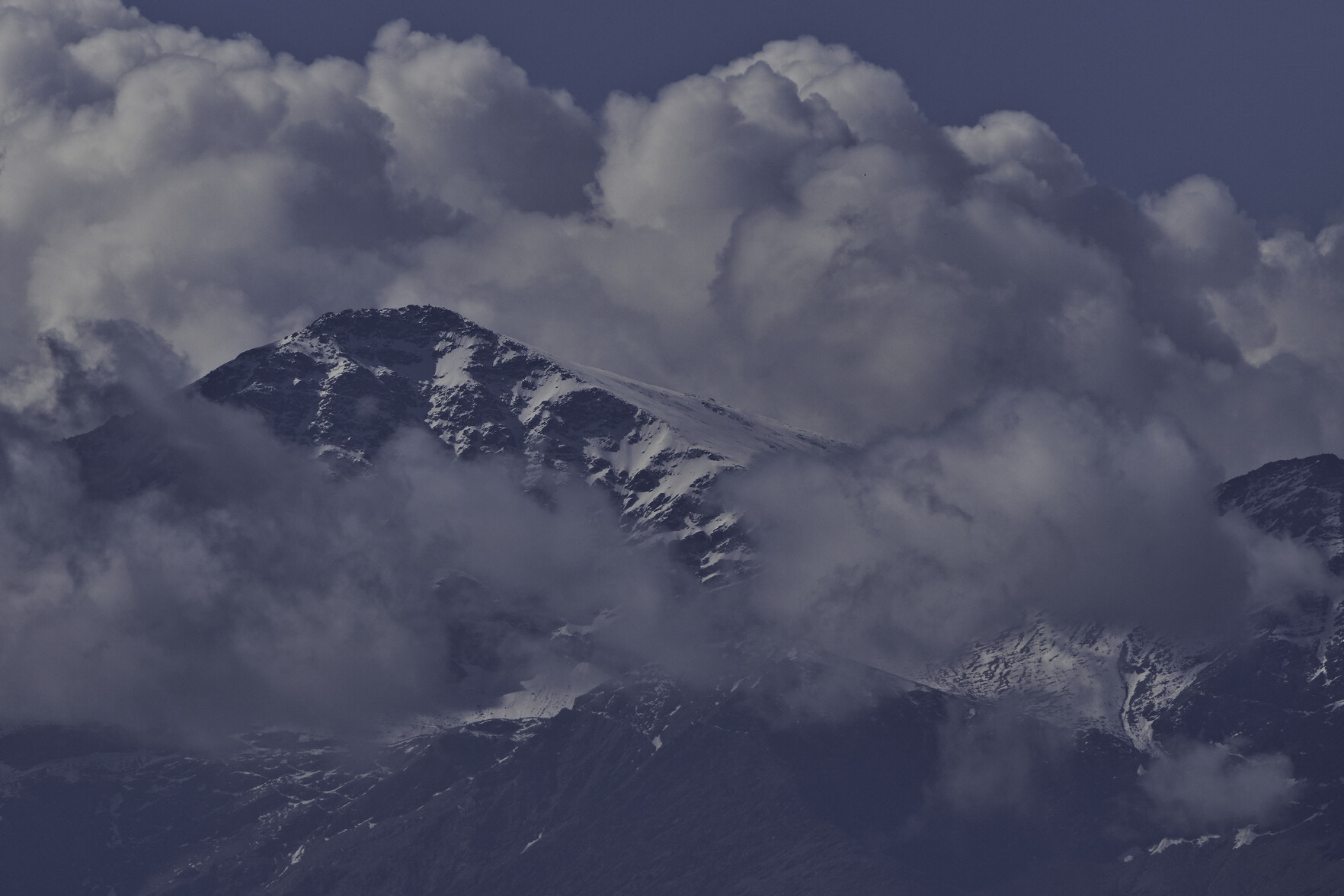 A mountain summit in snow emerges from the surrounding clouds