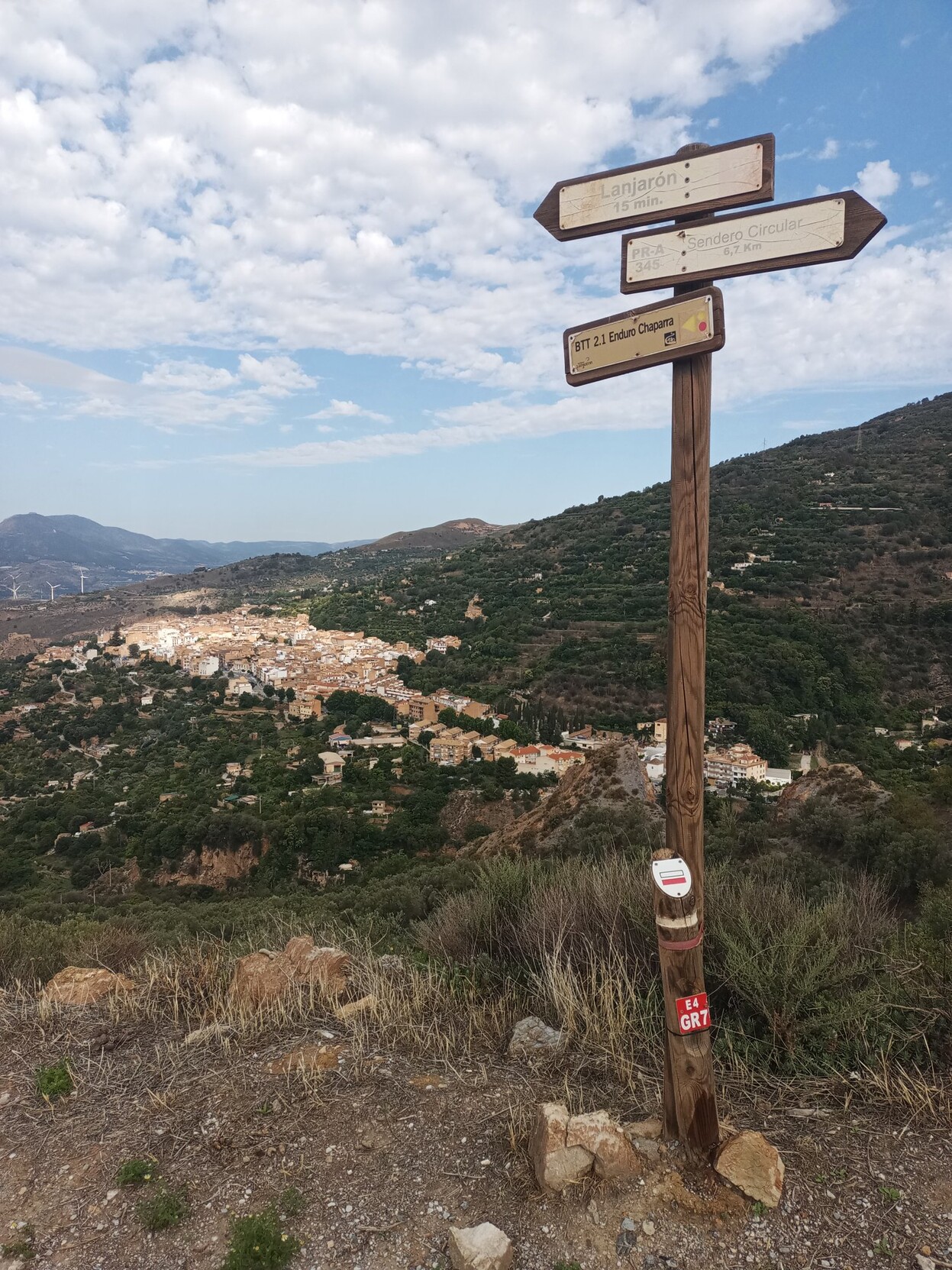 There is a hiking signpost with a town below in the background