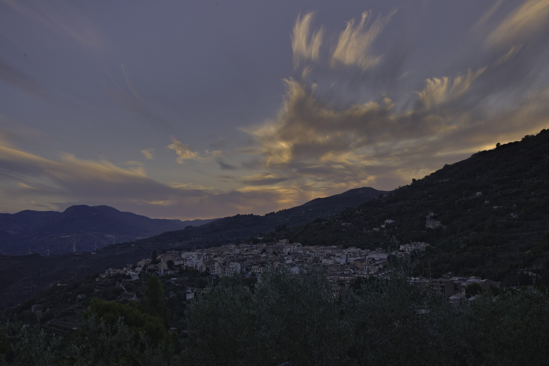 A small town in the foreground in the early evening dusk. Above colorful clouds formations