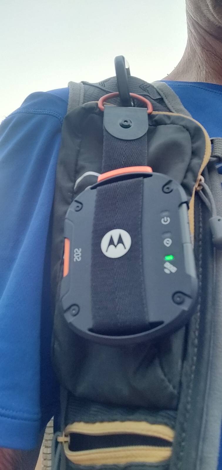 A hiker with blue shirt has a Motorola Defy Satellite Link clipped to his backpack strap