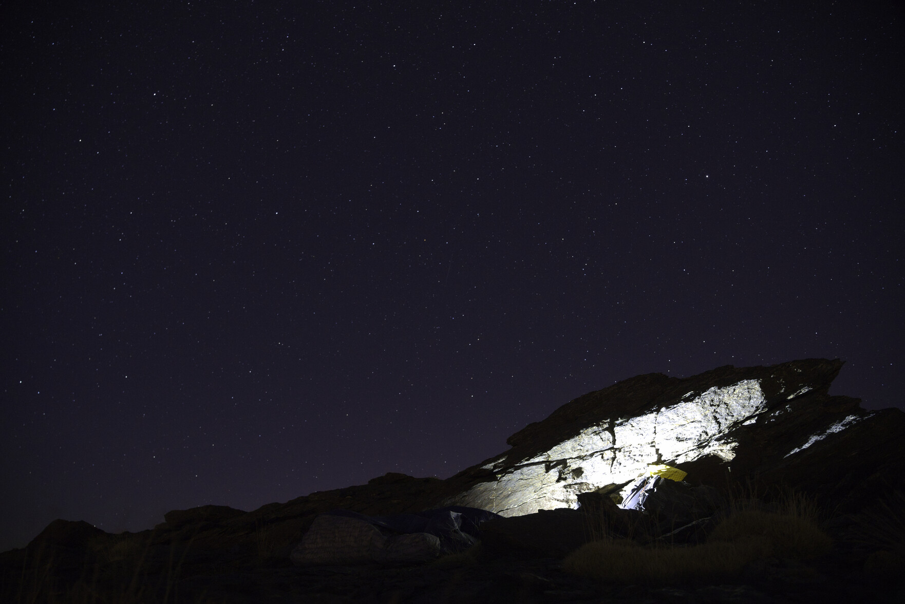 A dark sky filled with stars. To the bottom right there is a large rock illuminated by a head torch that shows where we slept