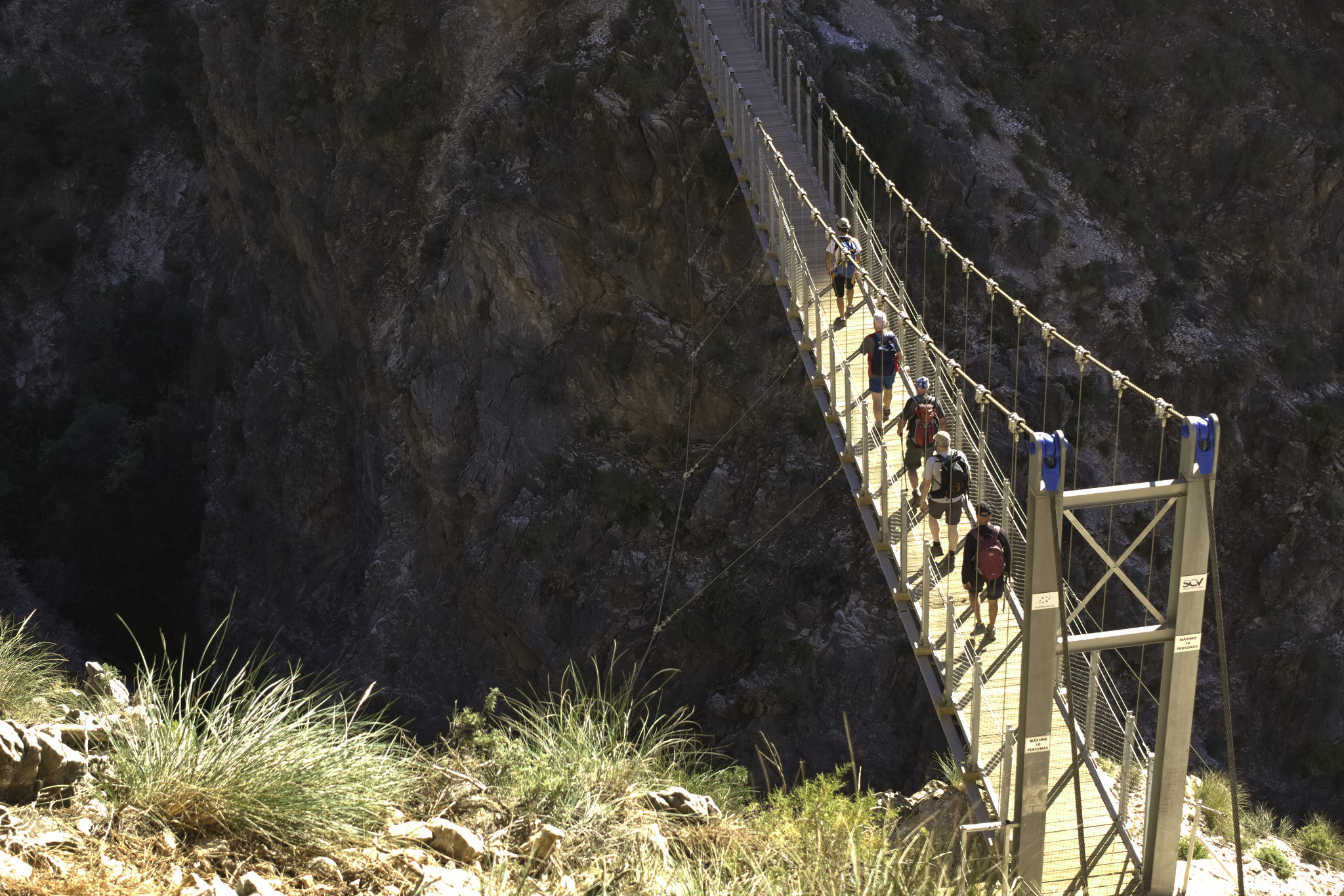 Hikers highlighted in morning the sun, cross a suspension bridge above a gorge