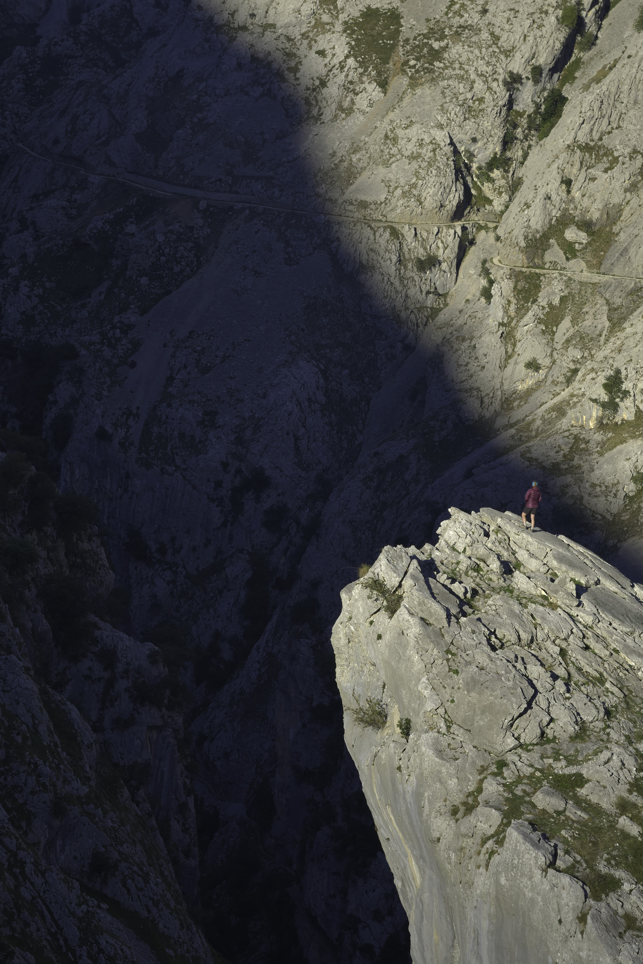 A figure with a purple jacket (my wife!) stands on a rock pinnacle illuminated by the early morning suns rays. The gorge is in deep shadow