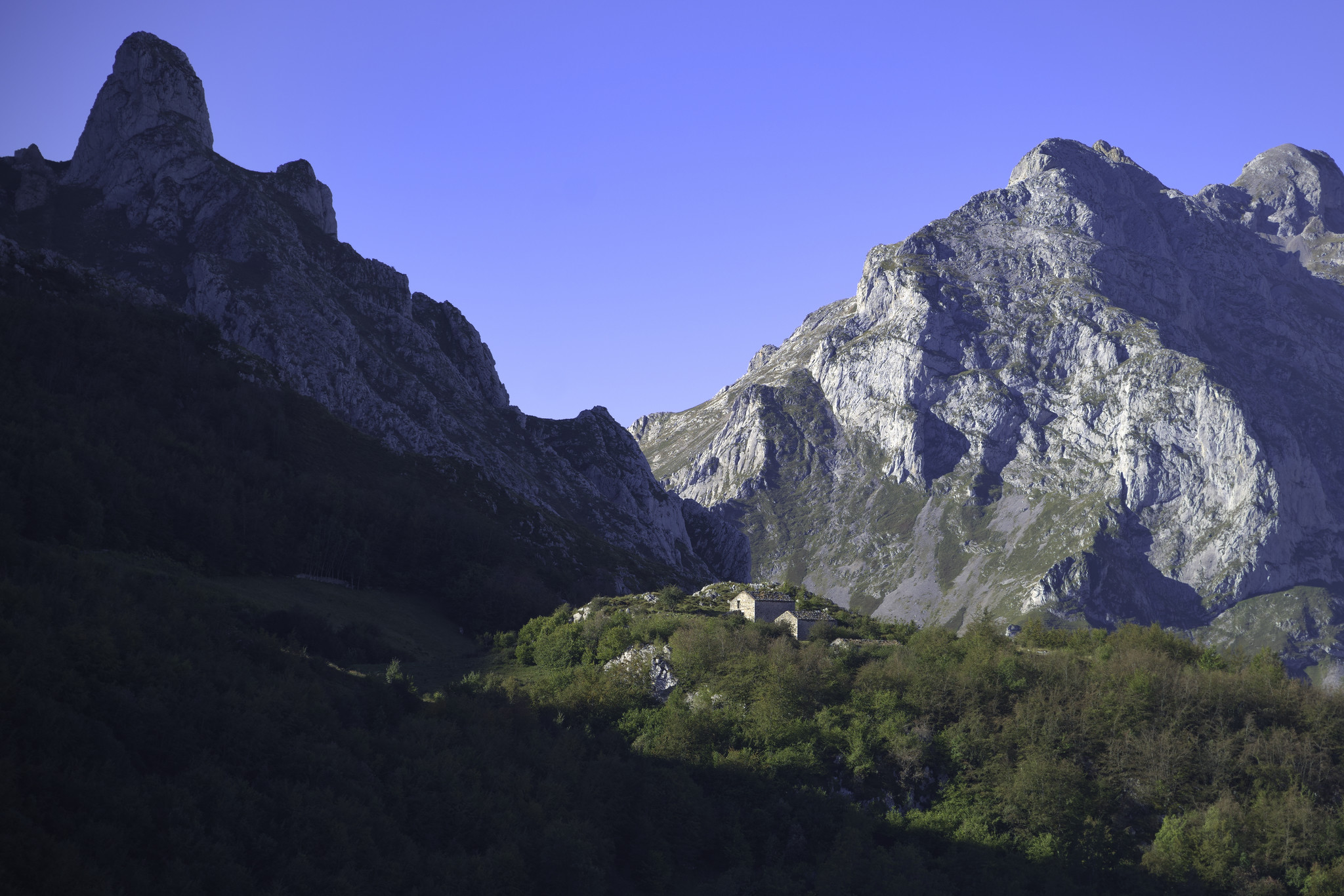 A huge shadowed peak soars up to the left. In the middle foreground lies a small hamlets of cabins sat in the trees