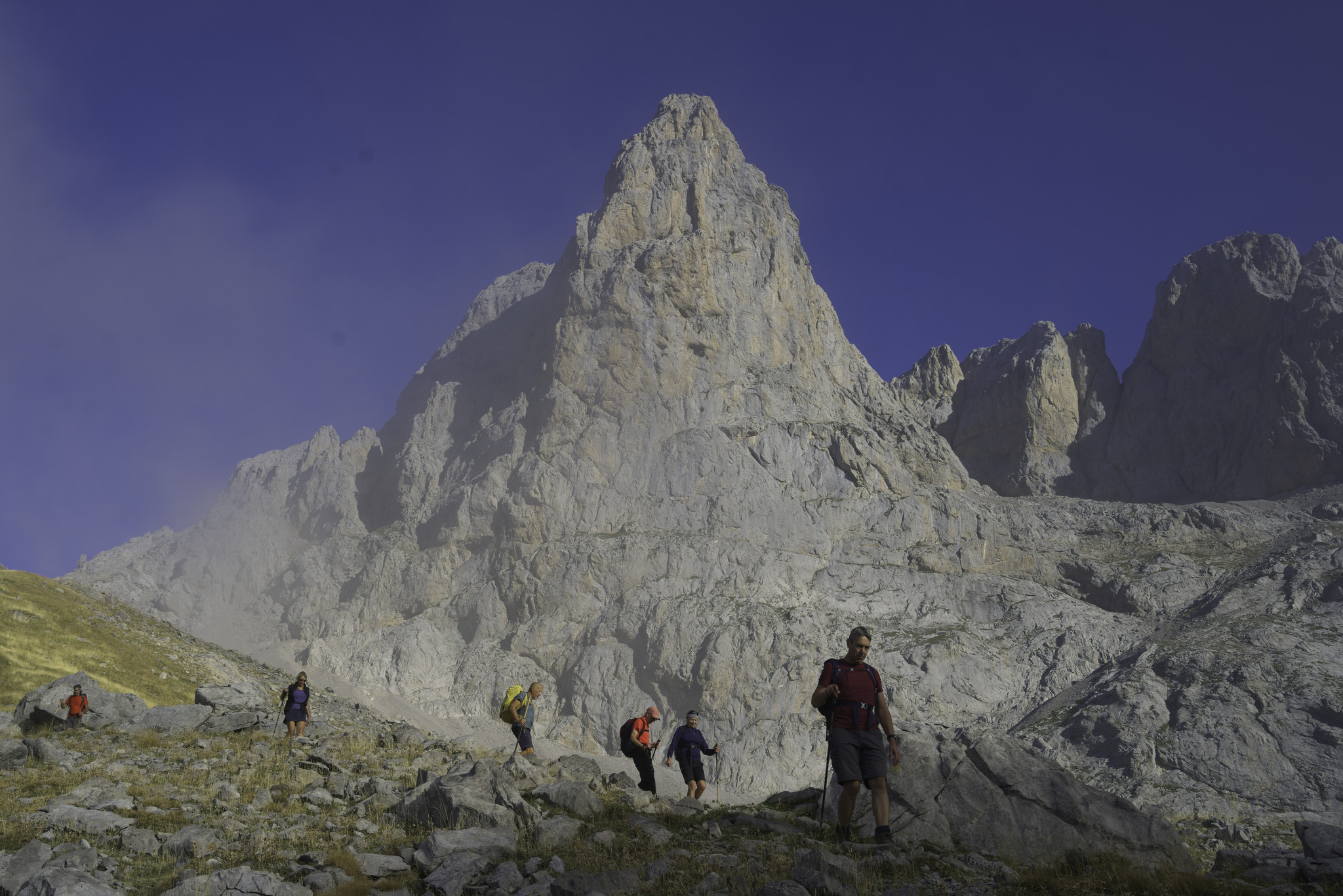 A spectacular gray and orange pyramid mountain (Torre de las Minas de Carbón 2483m) is at the back with some hikers passing in front in the foreground