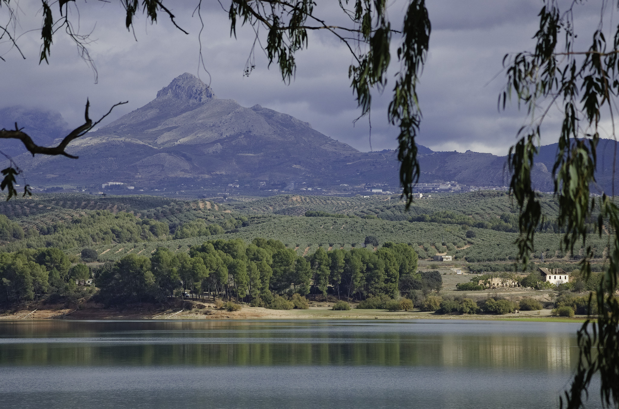 A lake is in the bottom. Above rises a mountain with a sharp rocky summit. Dark clouds above