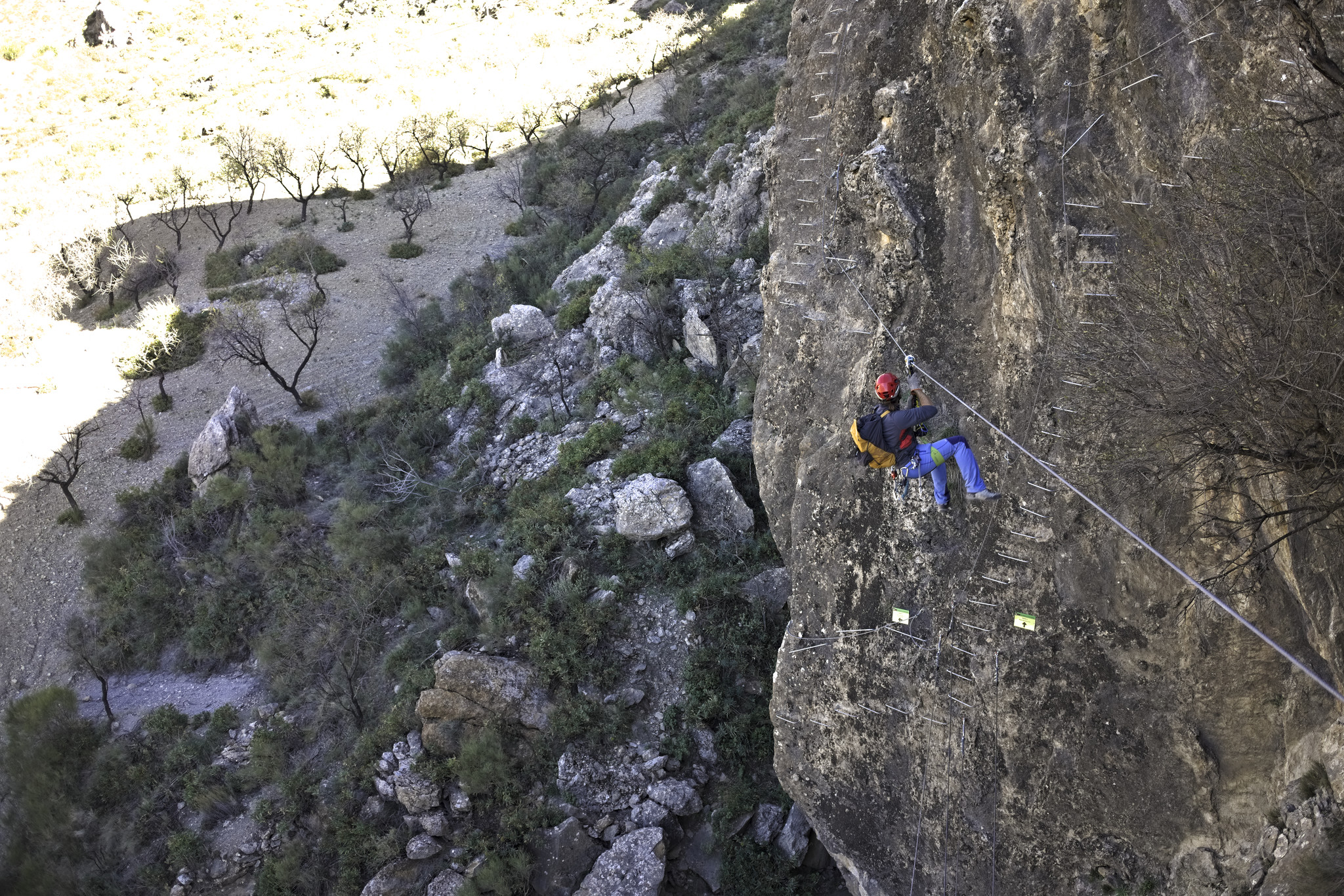 A person crosses a tyrolean zip line across a gorge with some steps into the wall at the end