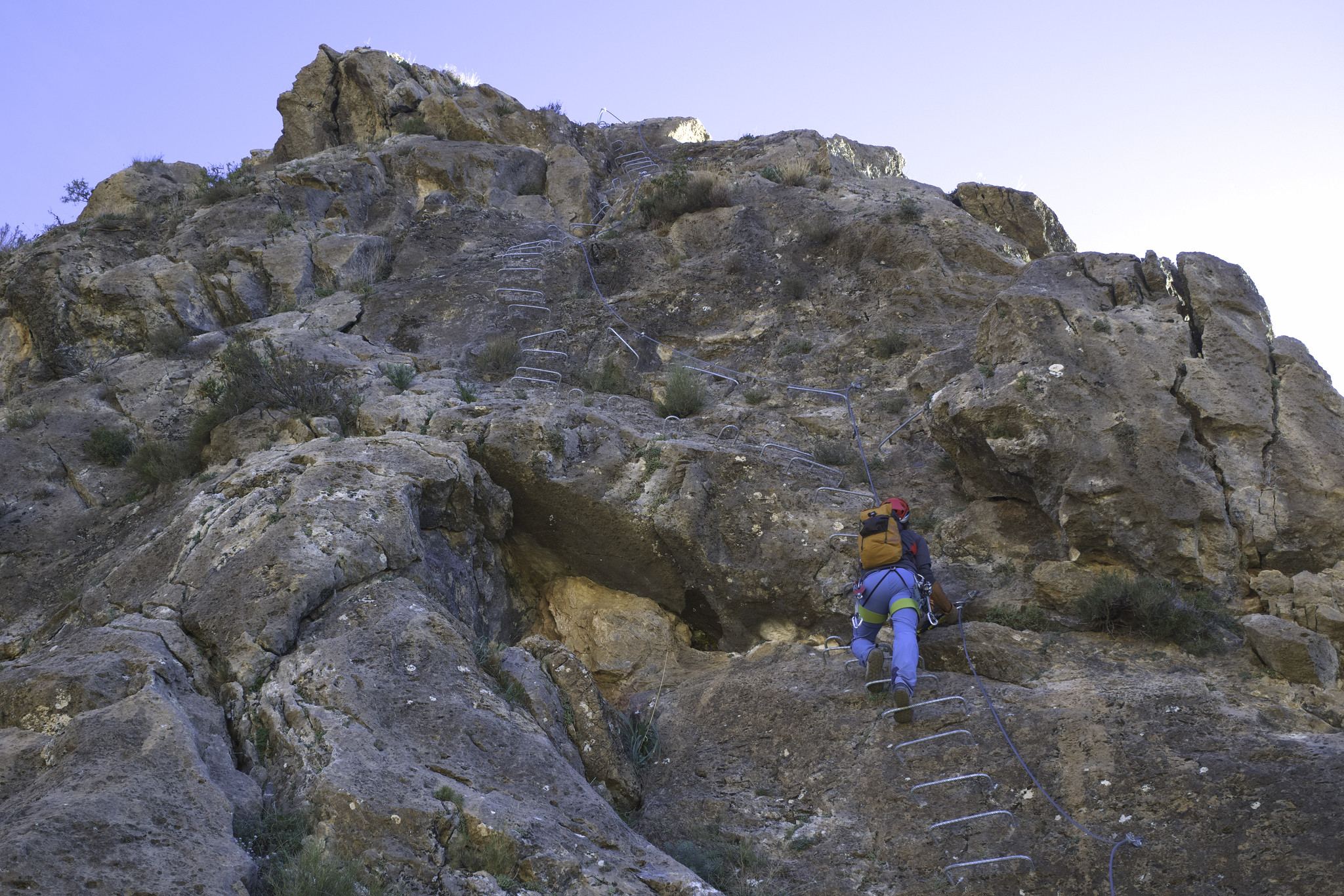 A person ascends rungs of a via ferrata secured by chains and cables