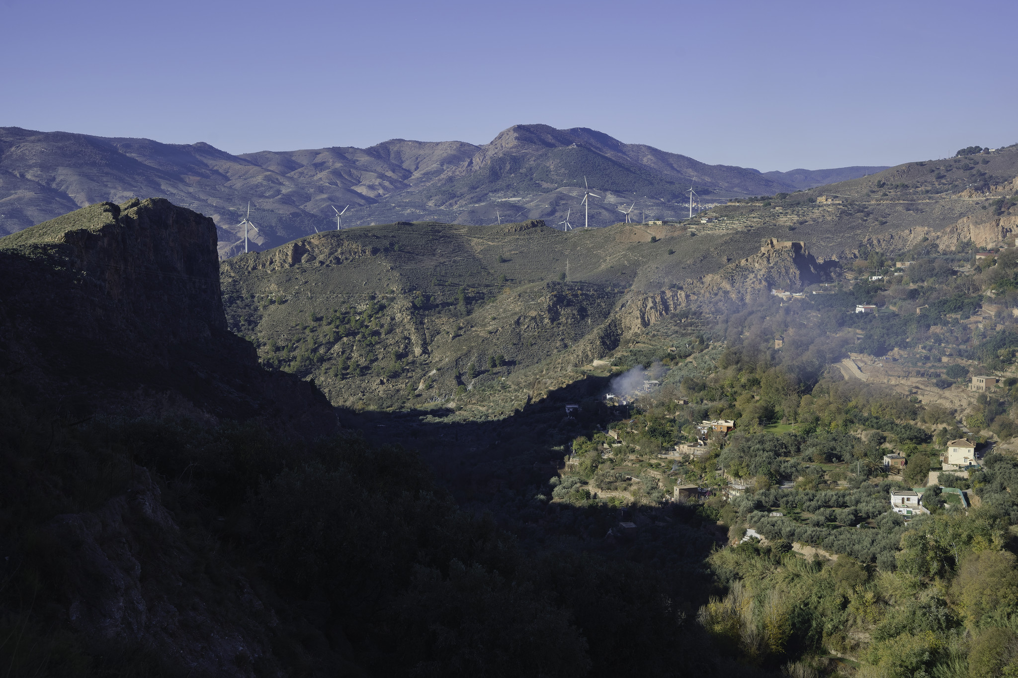 The morning sun illuminates the to and right of the image which shoes green fields and hillsides. The left has some steep cliffs in dark shadow