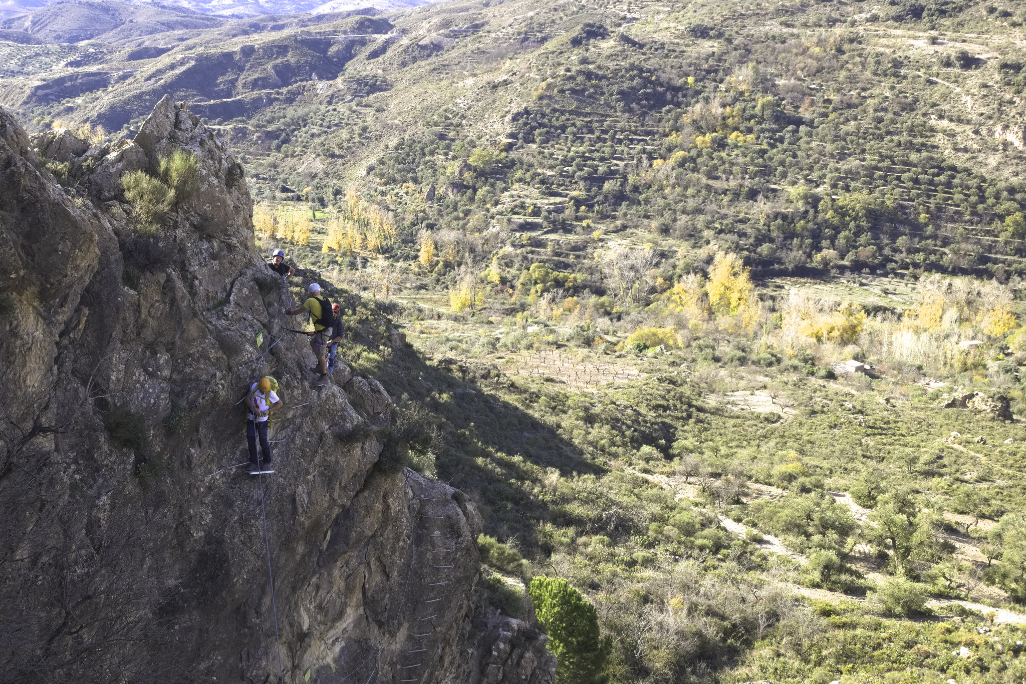 Some people are climbing up or rock wall equipped with ladders and are using cables for protection