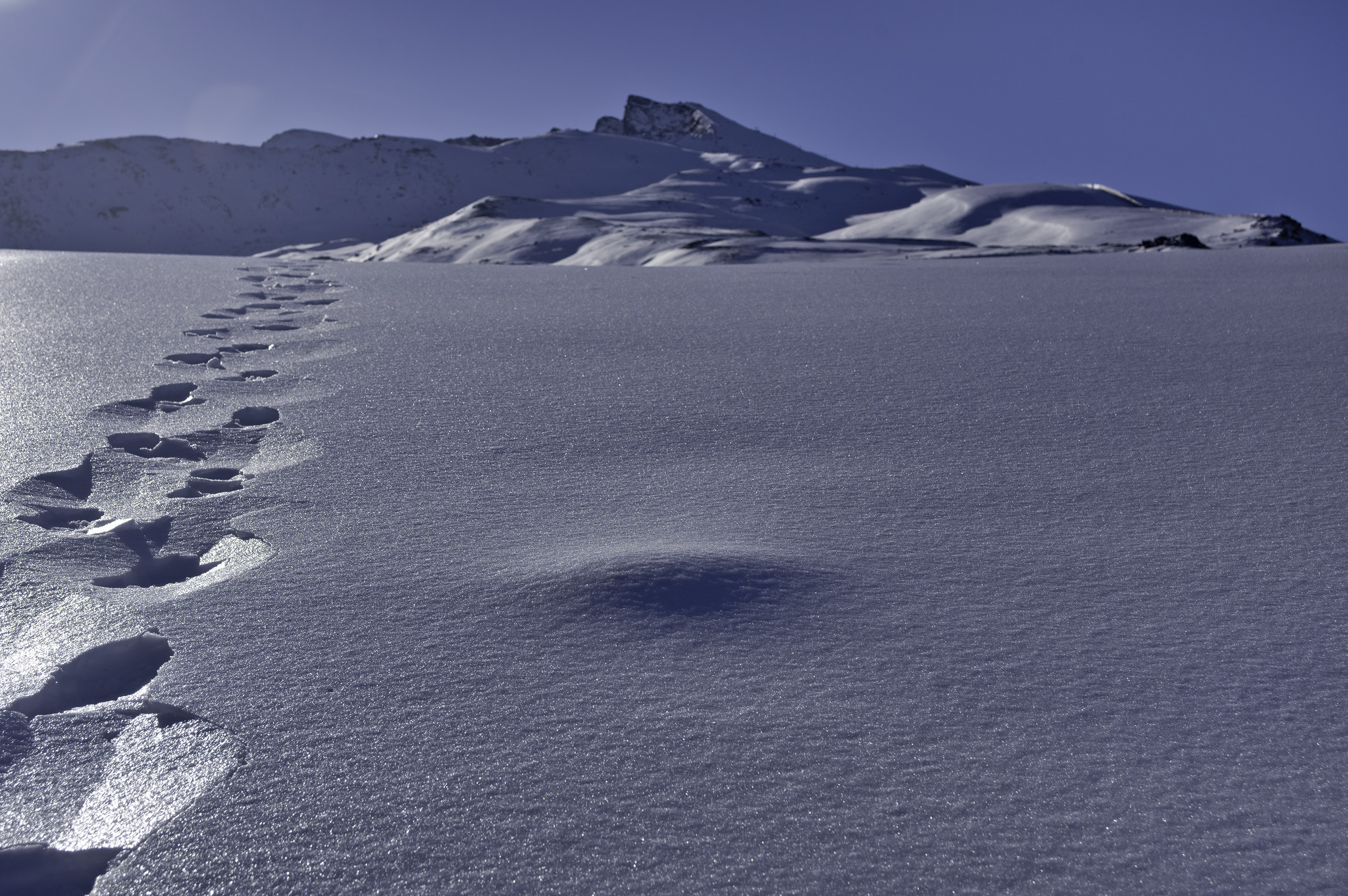 Tracks in the snow on the left lead up to a mountain summit