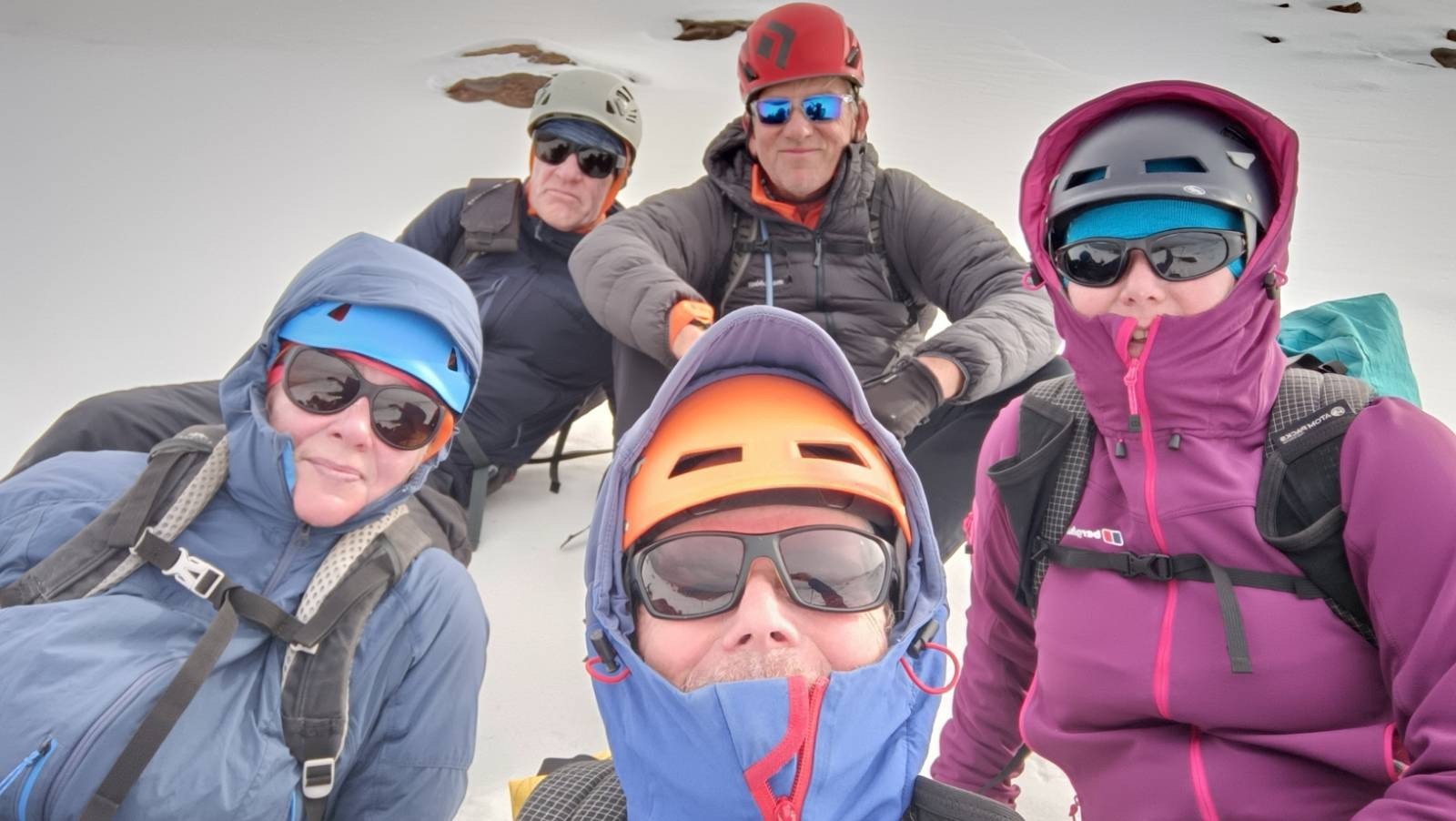 5 people all with helmets and dark glasses it in the snow in the mountains