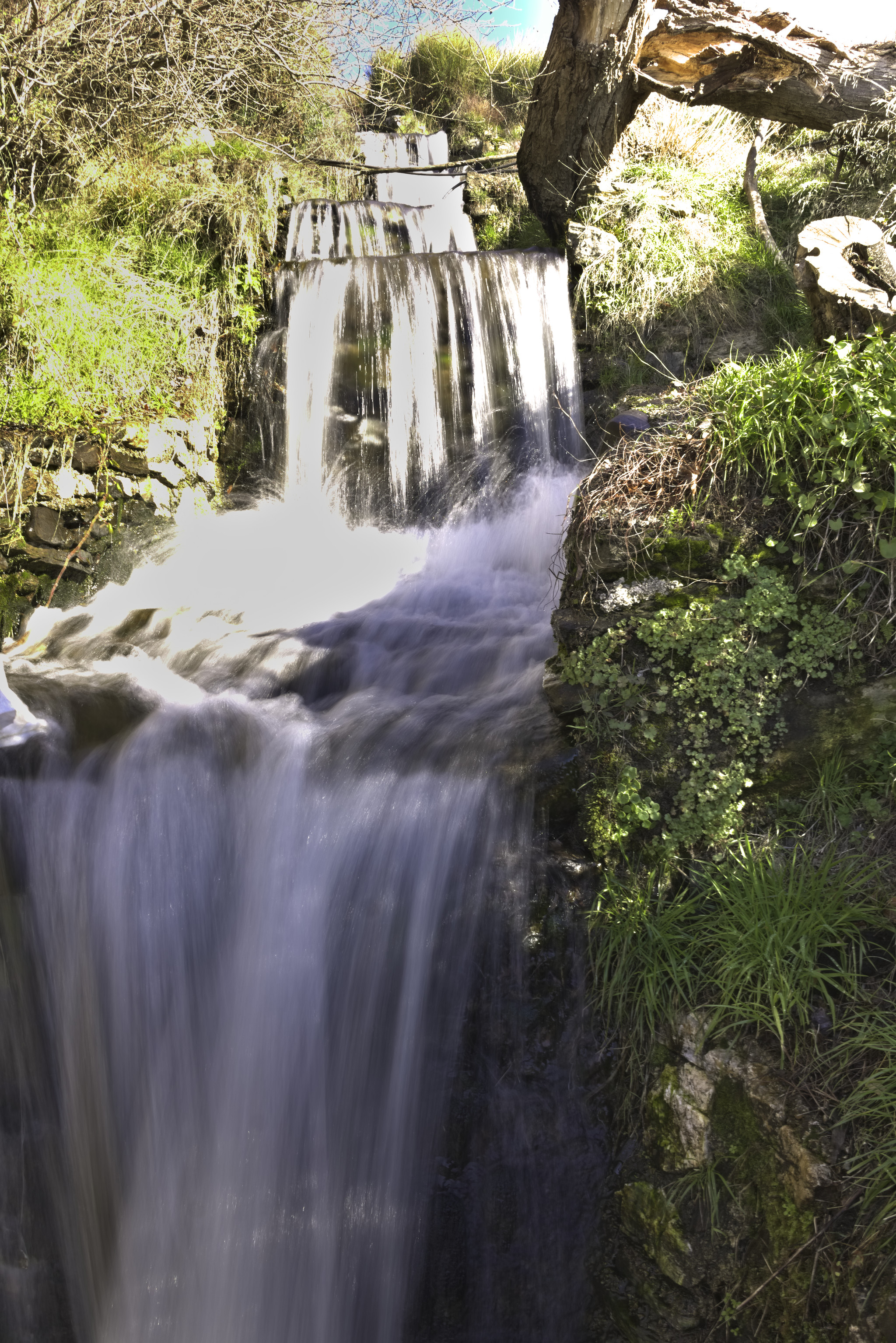 Some waterfalls drop down various short steps whilst lush green shrubs line the sides of the flow