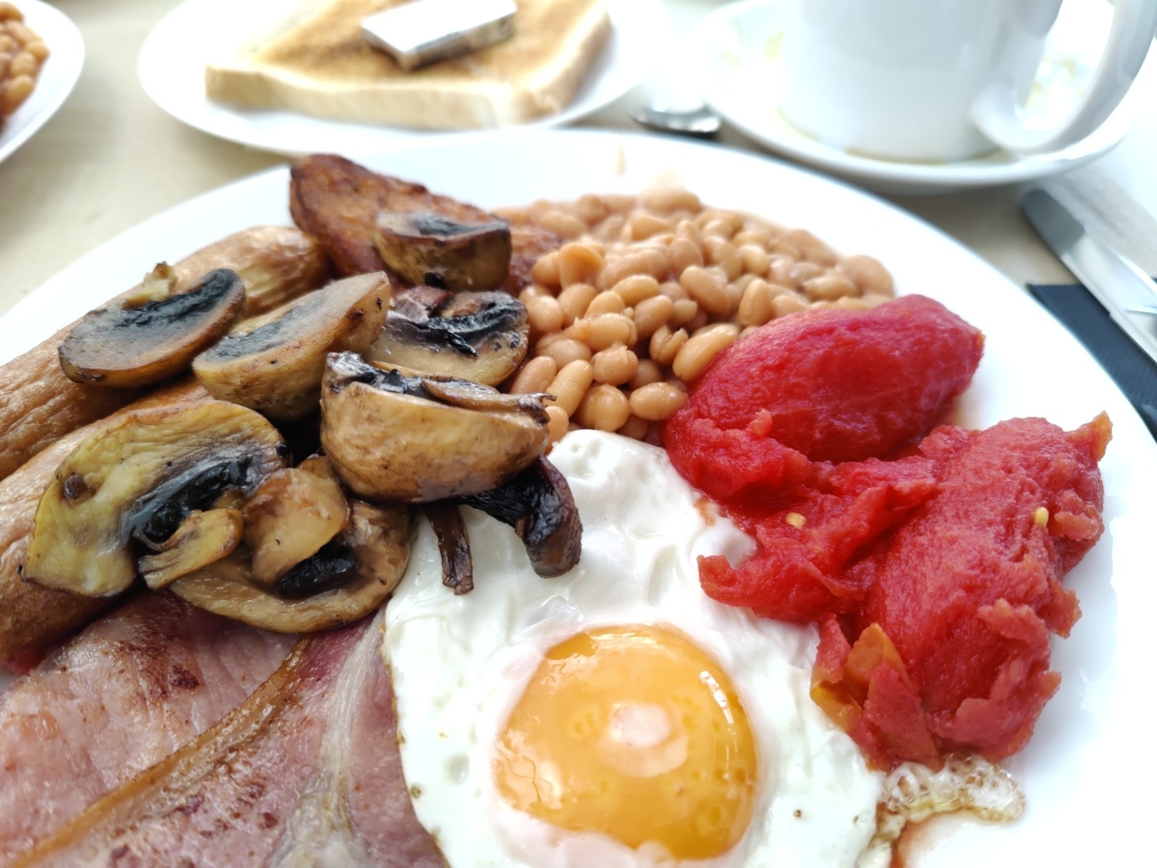 A plate of typical engligh breakfast food. Egg, bacon, tomato, mushroom, beans and sausage