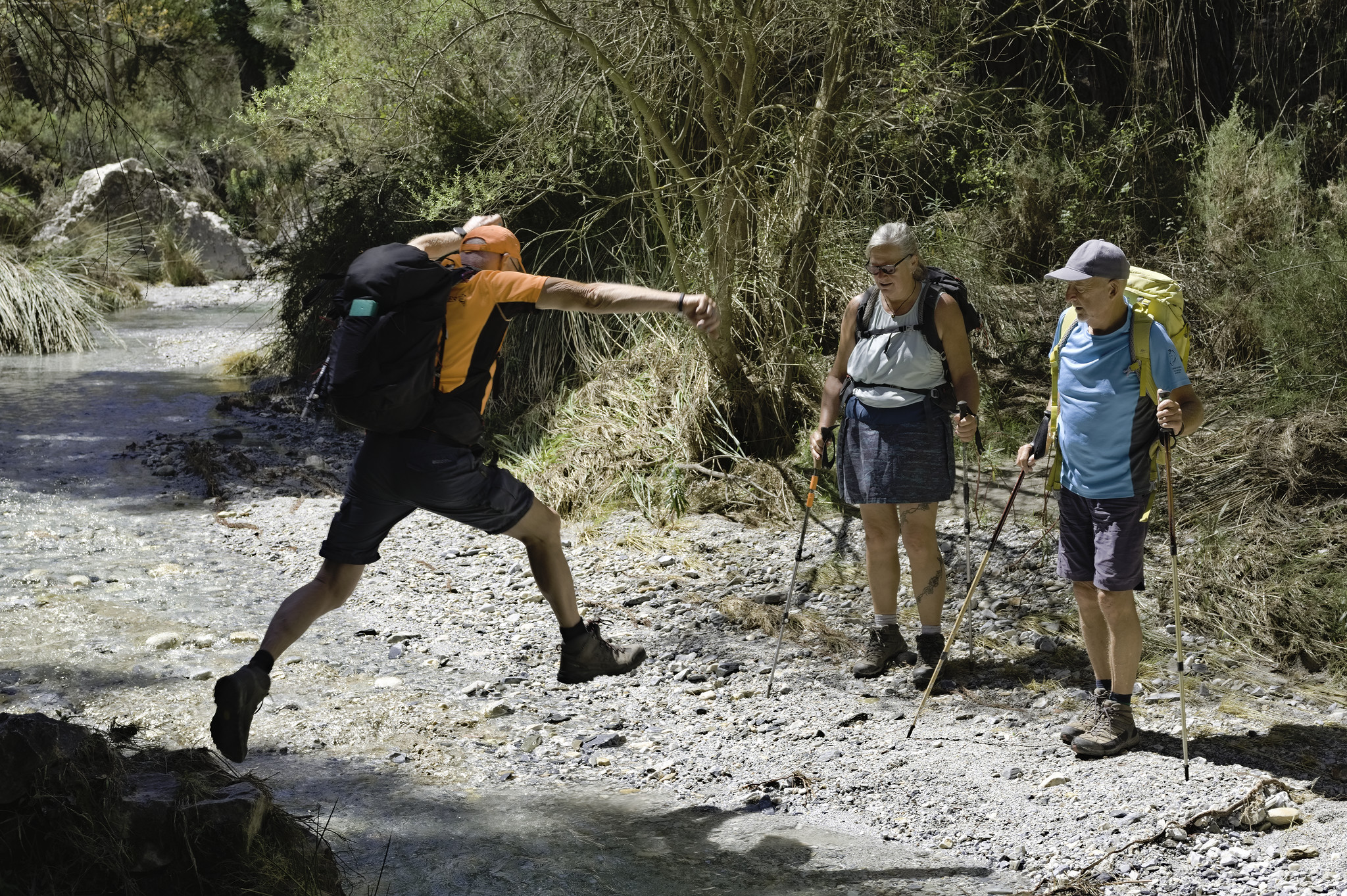 A person jumps across a small stream hoping not to get his feet wet! Two other stand watching with anticipation!