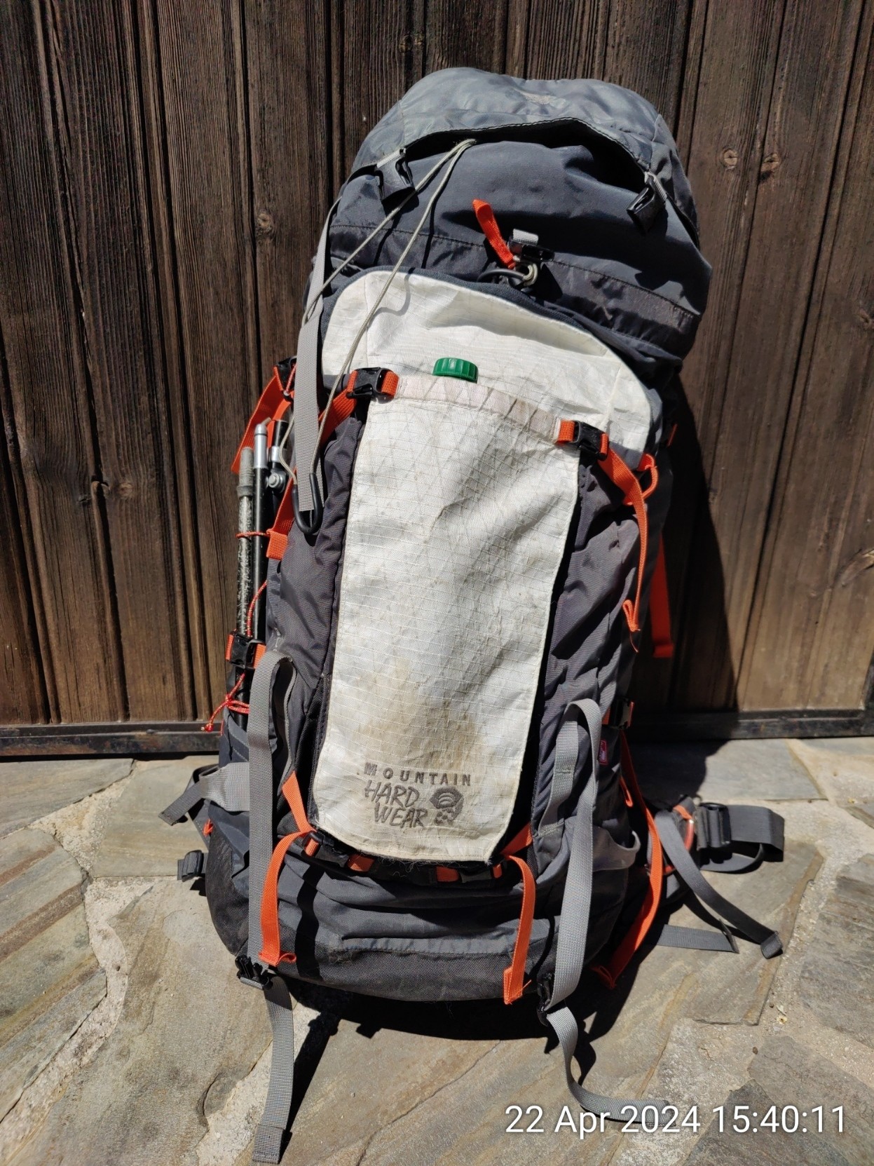 A white and grey Mountain Hardware backpack with orange tags, sits against an old wooden fence