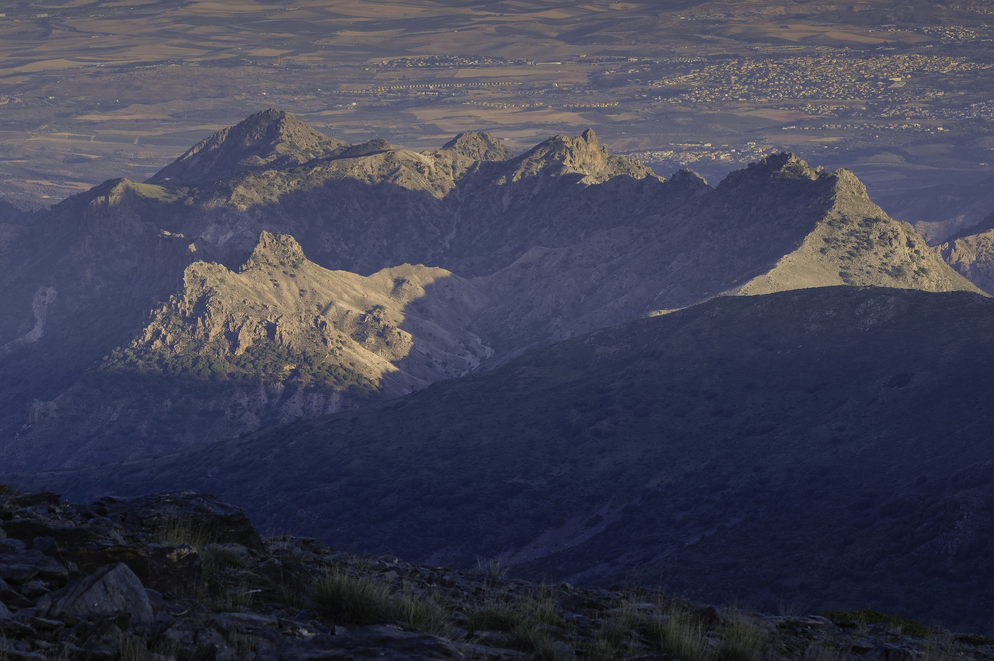 Some jagged mountains are bathed in early morning light whilst the foreground is in shadow. At the back to the right is a town