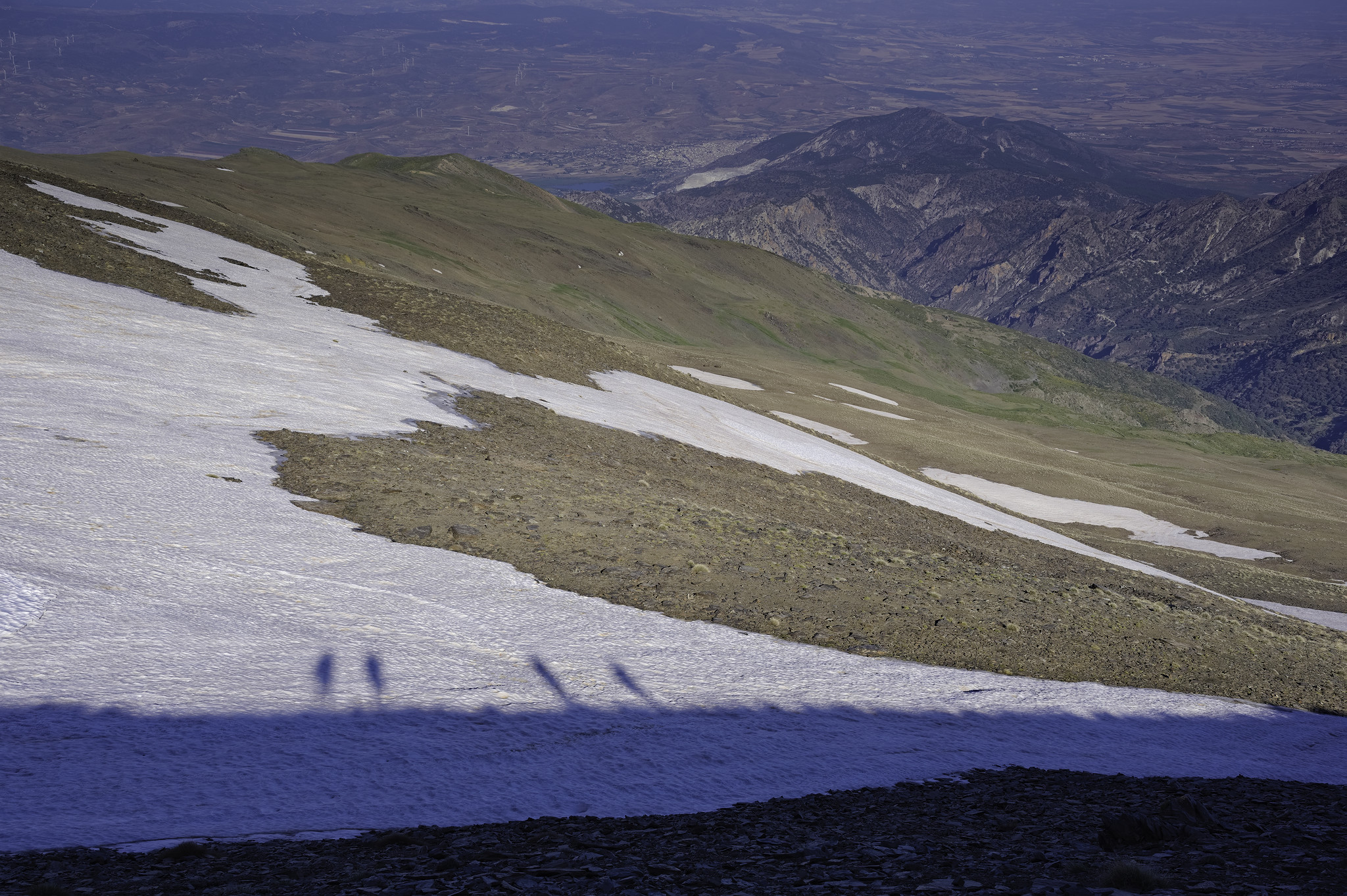 The shadow of 4 hikers is seen reflected in some white snowfields 