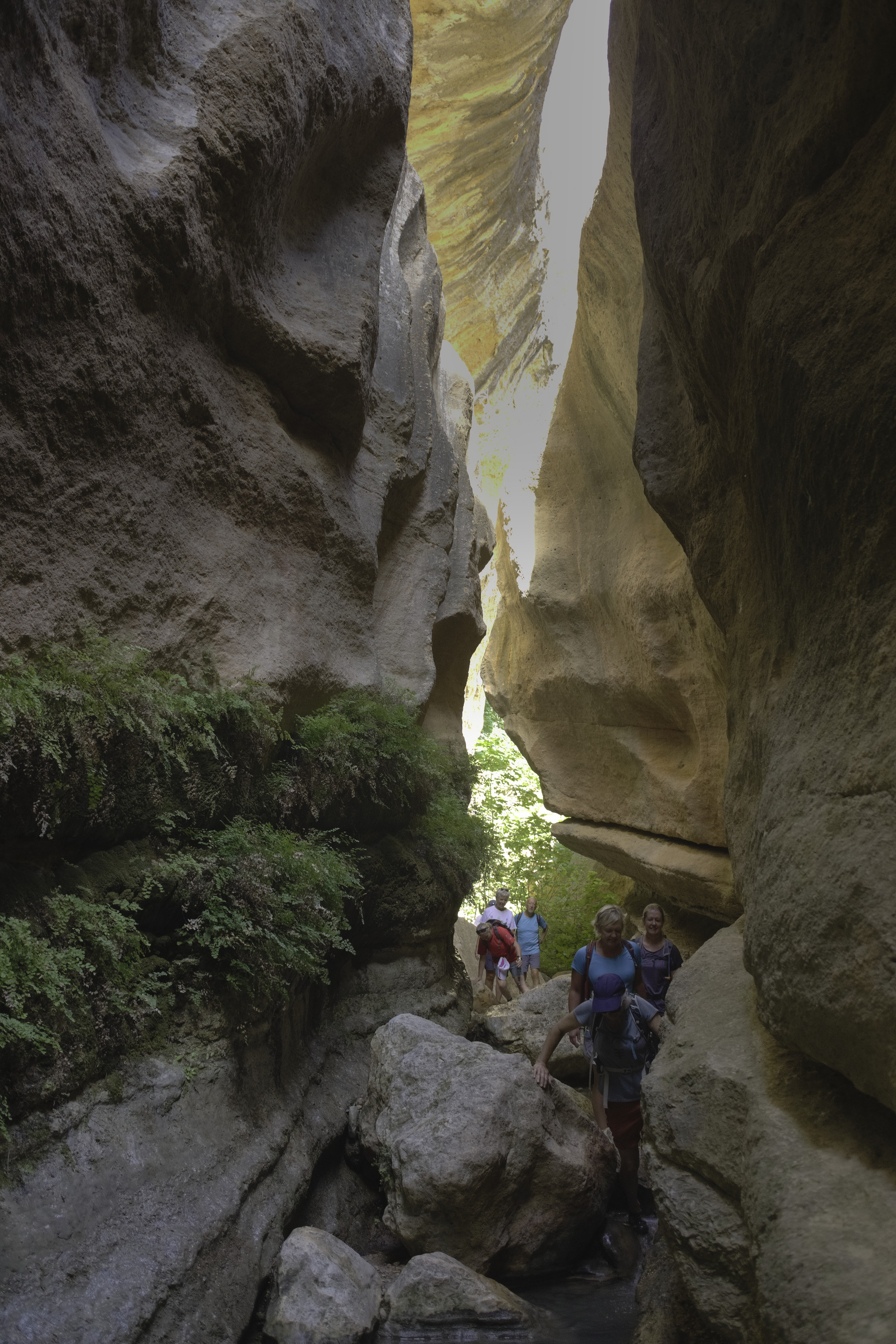 A group of people pass down a narrow gorge that is illuminated above by the morning sun