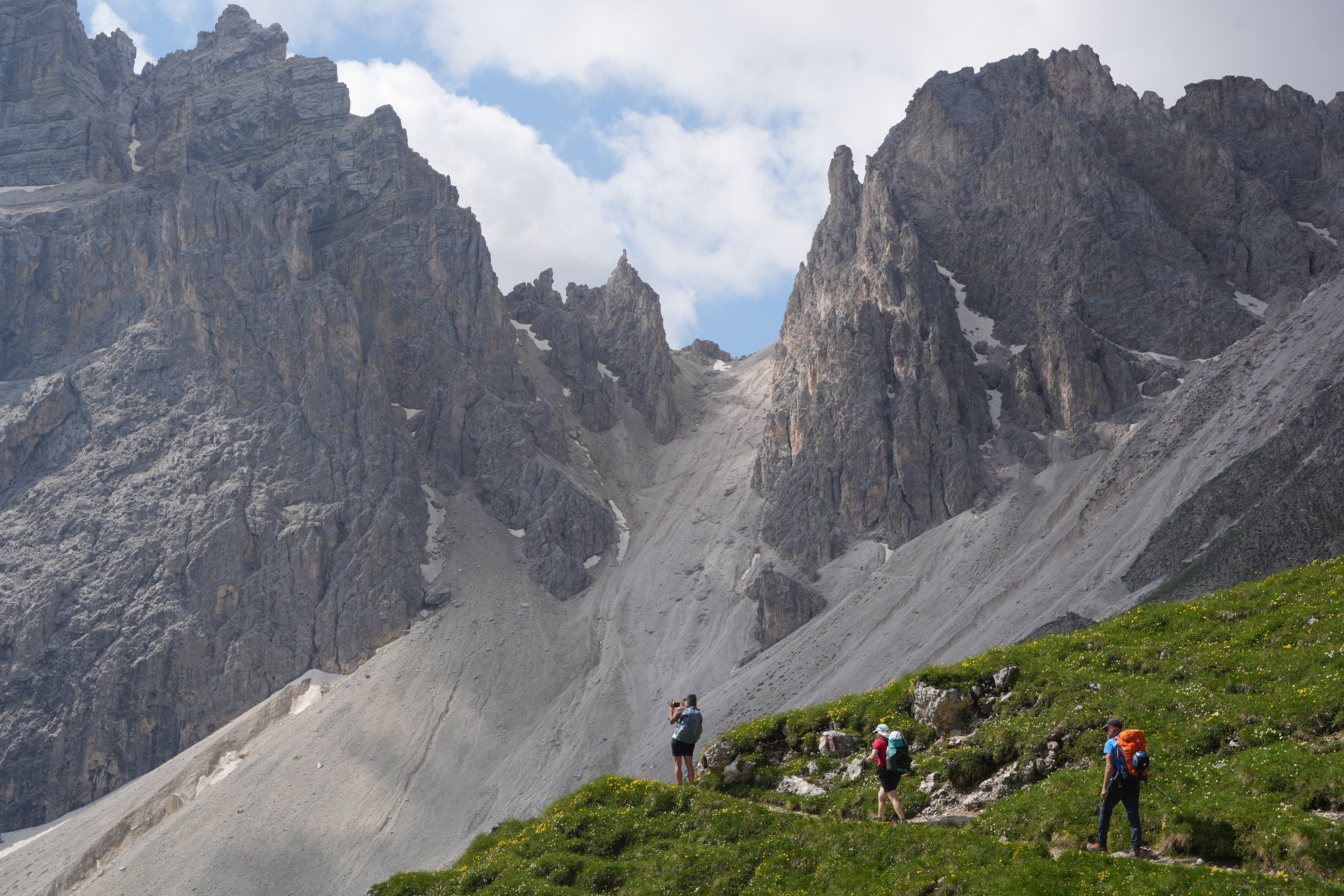 Hikers on a path below a pass surrounded by mountains