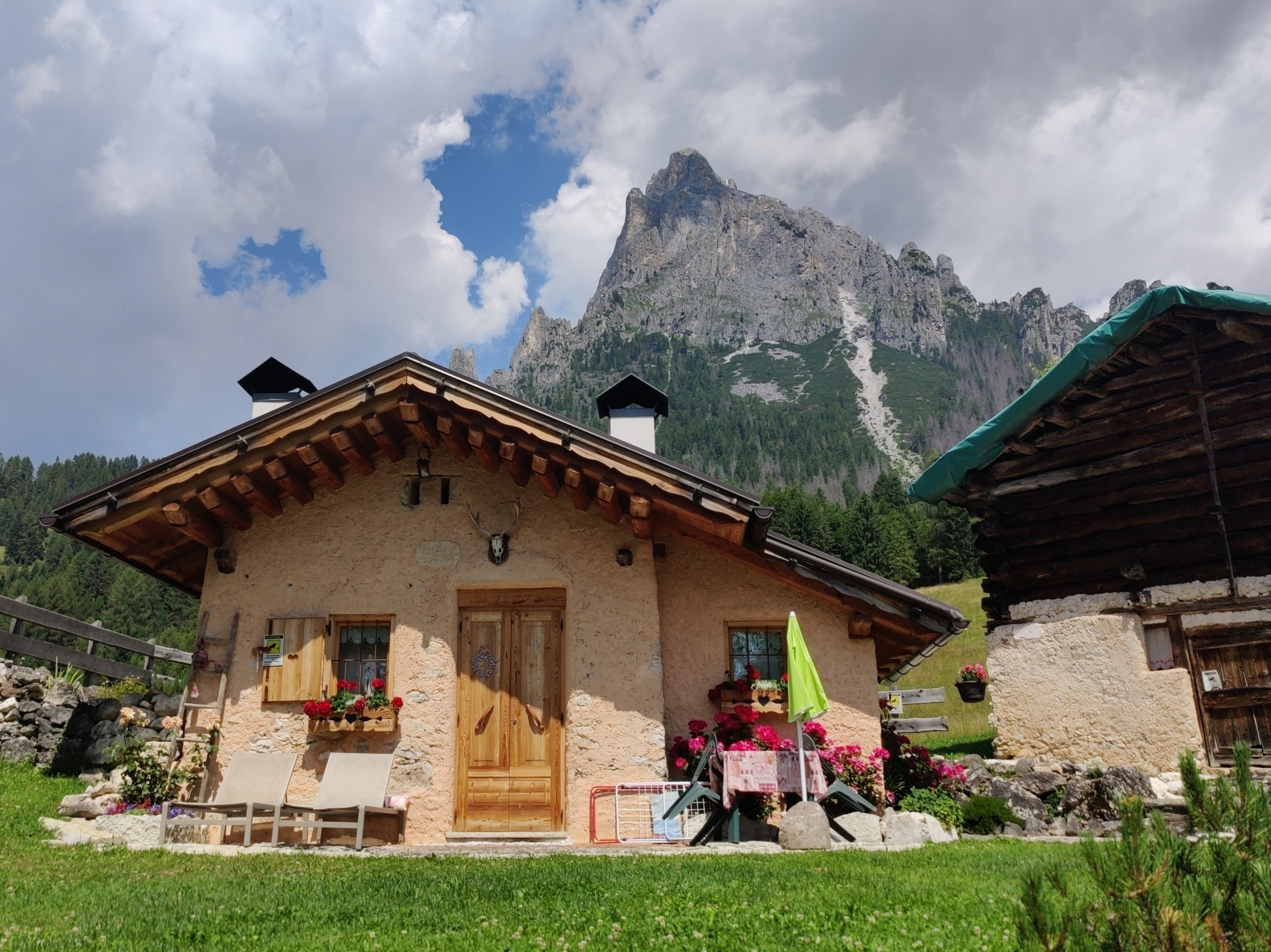 A pretty alpine cuckoo clock house sits on. a green field with a huge mountain riding behind