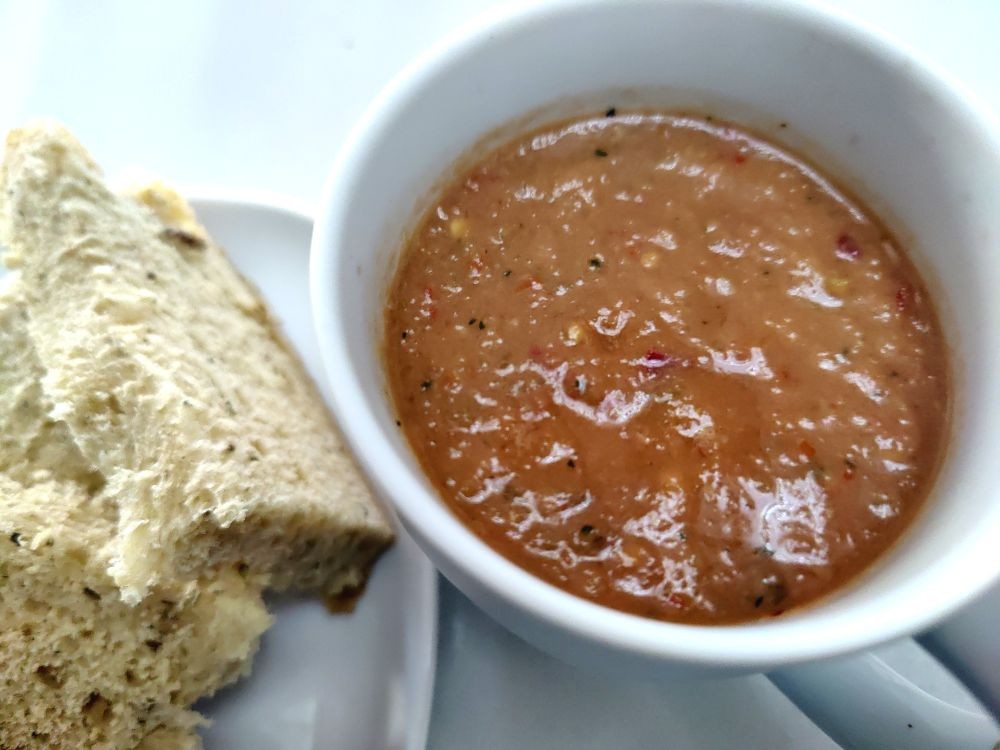 A bowl of gazpacho soup sits next to some chunks of home made bread