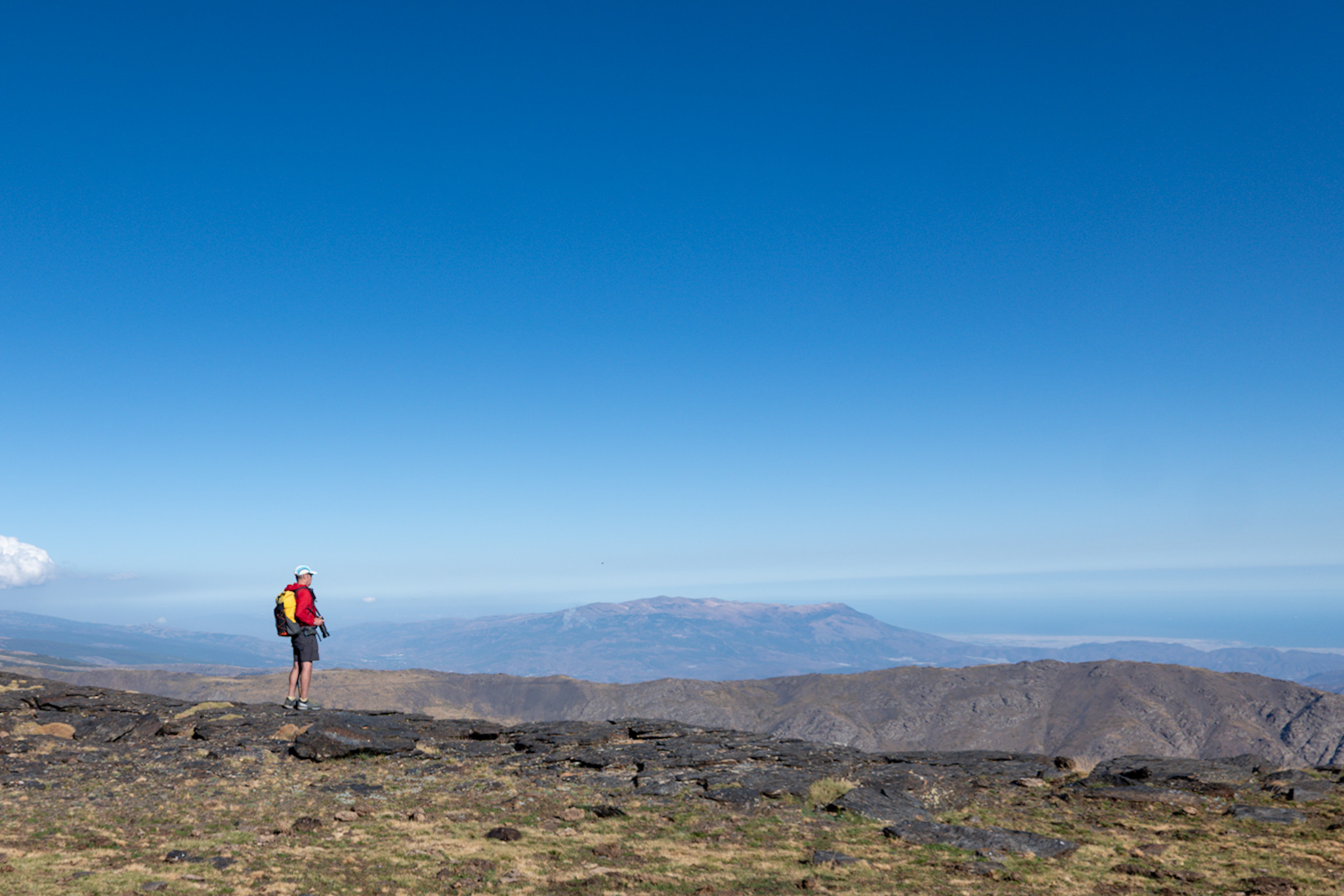 A person with red jacket stands looking out at some mountain ranges