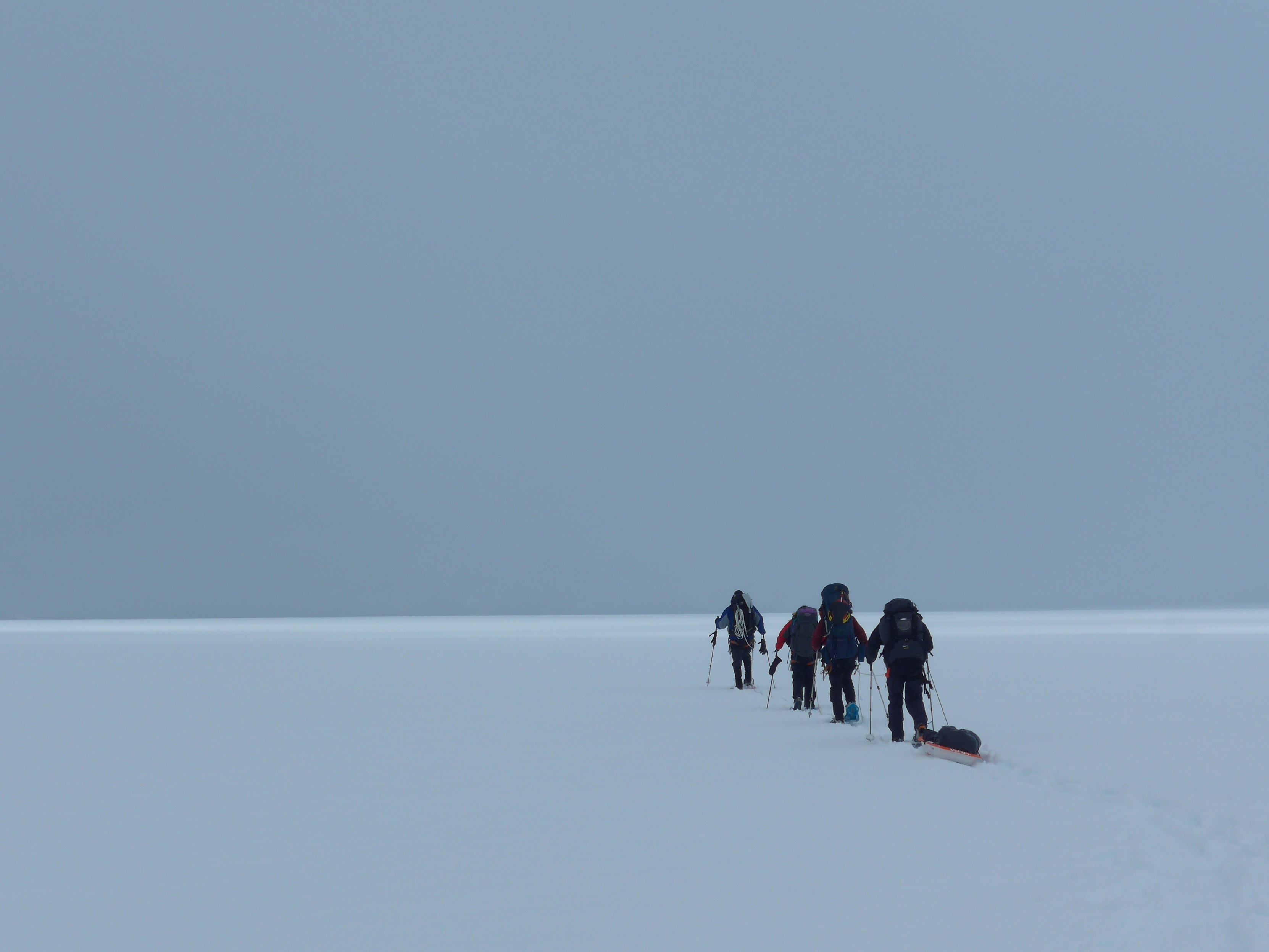 A group pull a sledge over a flat glacier with grey cloud above