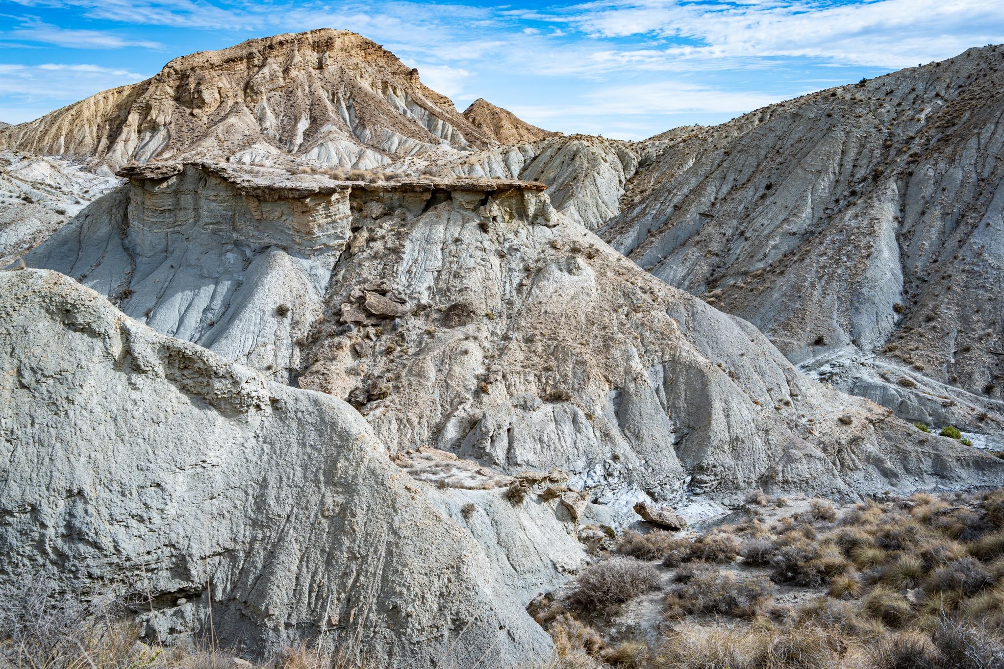 An arid desert badlands scene with a chaotic mass of broken rock and battered, crumbling cliffs