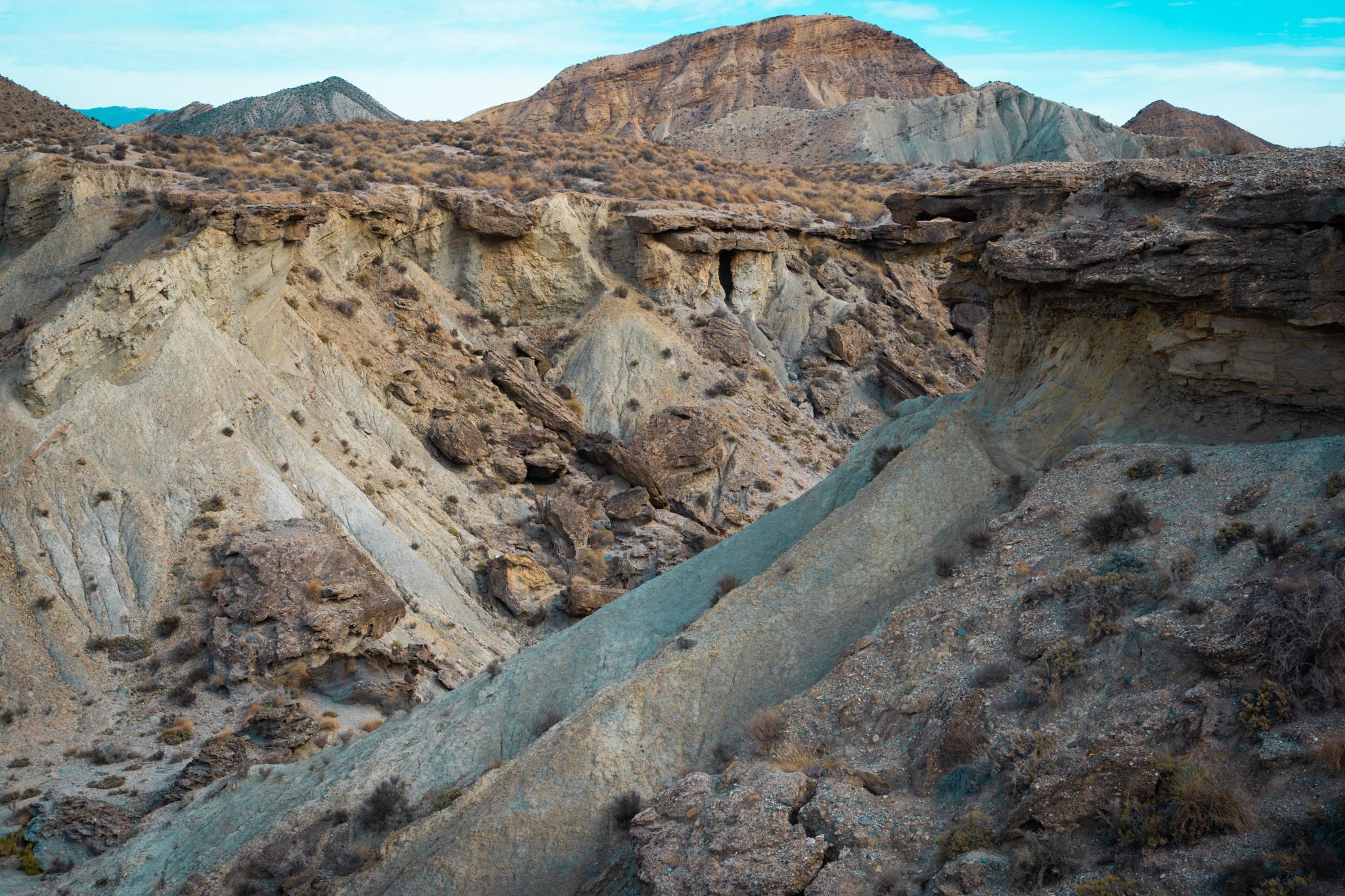 An arid desert badlands scene with a chaotic mass of broken rock and battered, crumbling cliffs