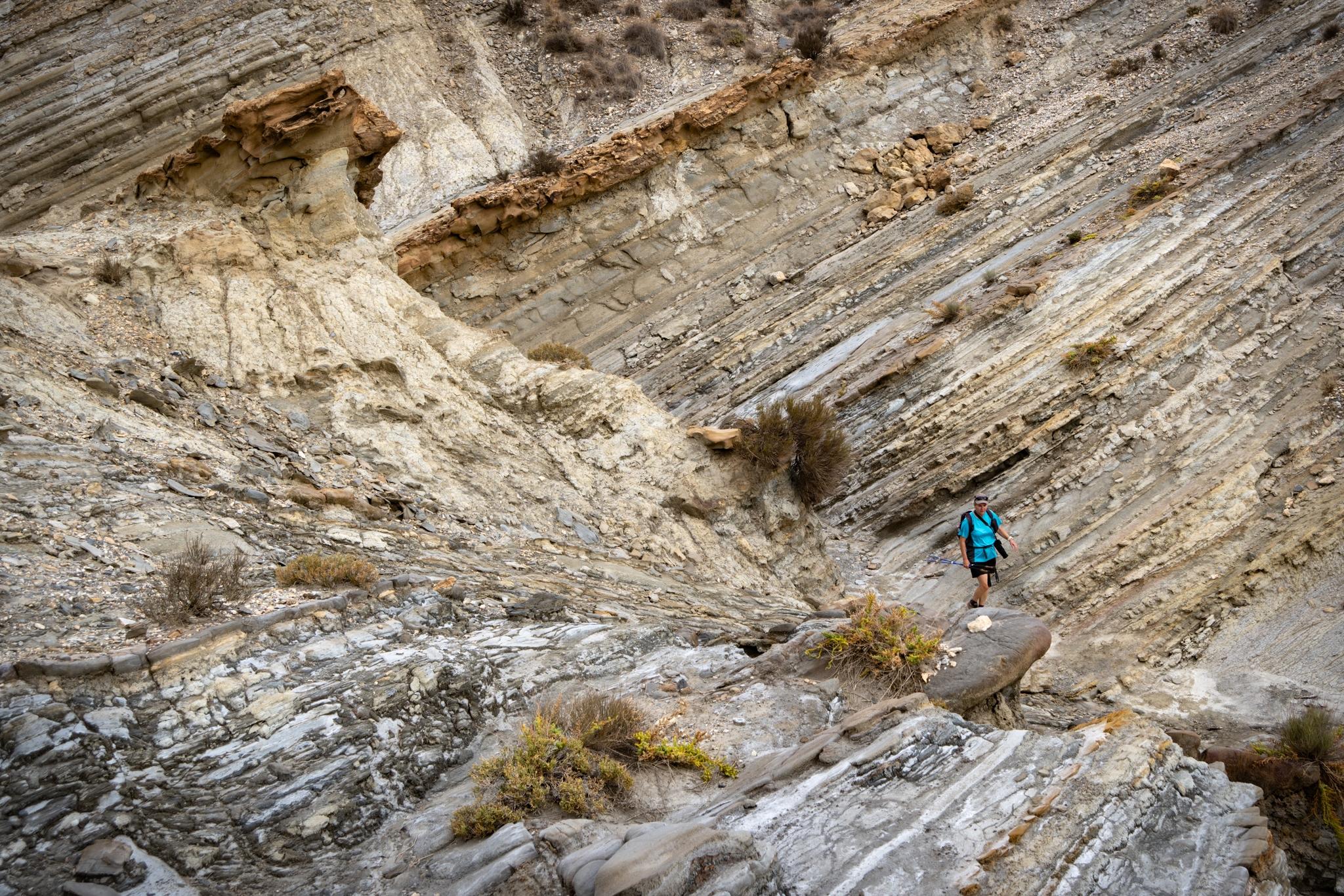 A person in blue walks through a valley with striated rock formations