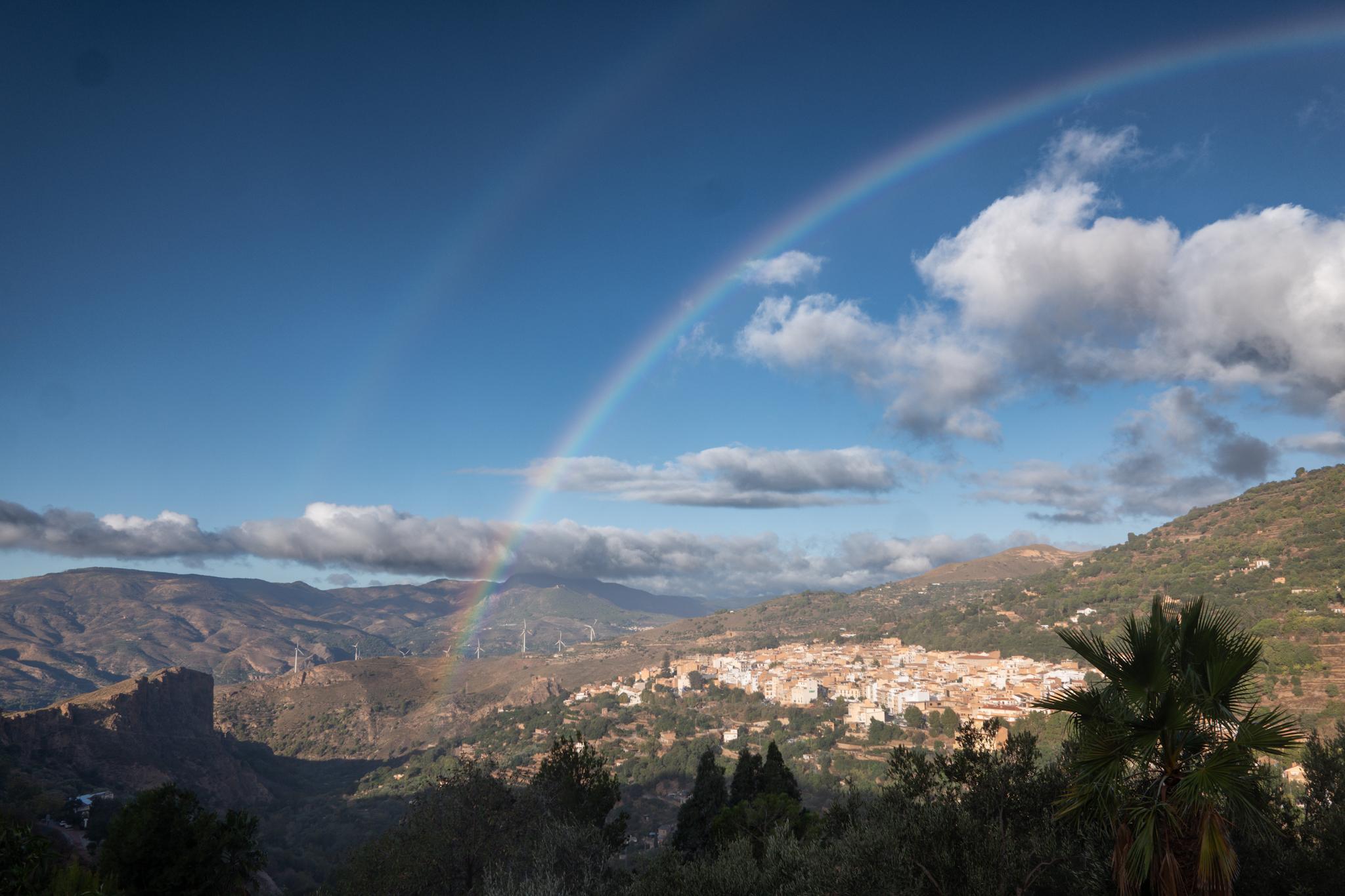 A rainbow sits above a spanish town. Blue sky day.