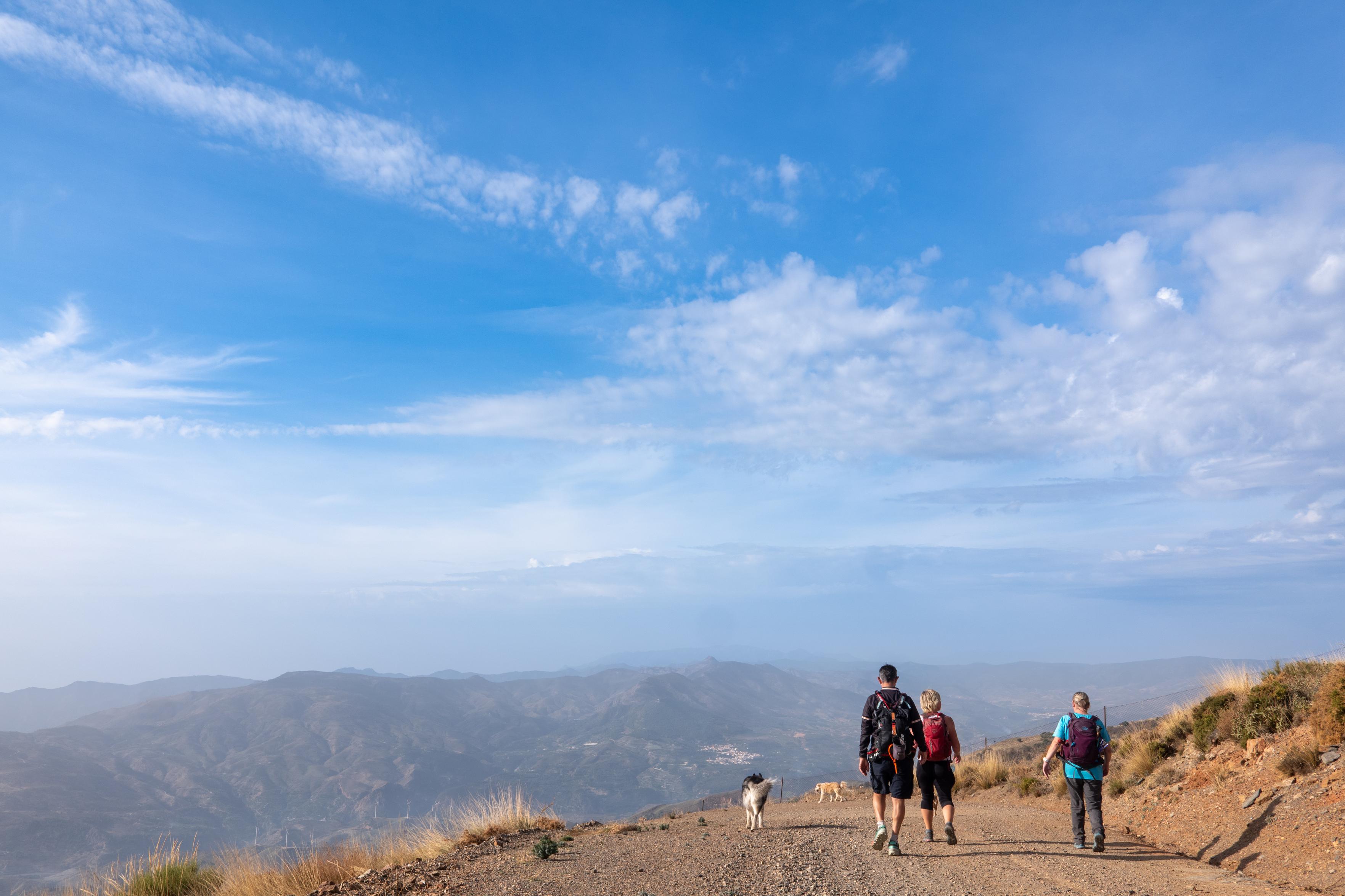 People walking along a wide dirt road with open skies of blue with white cloud