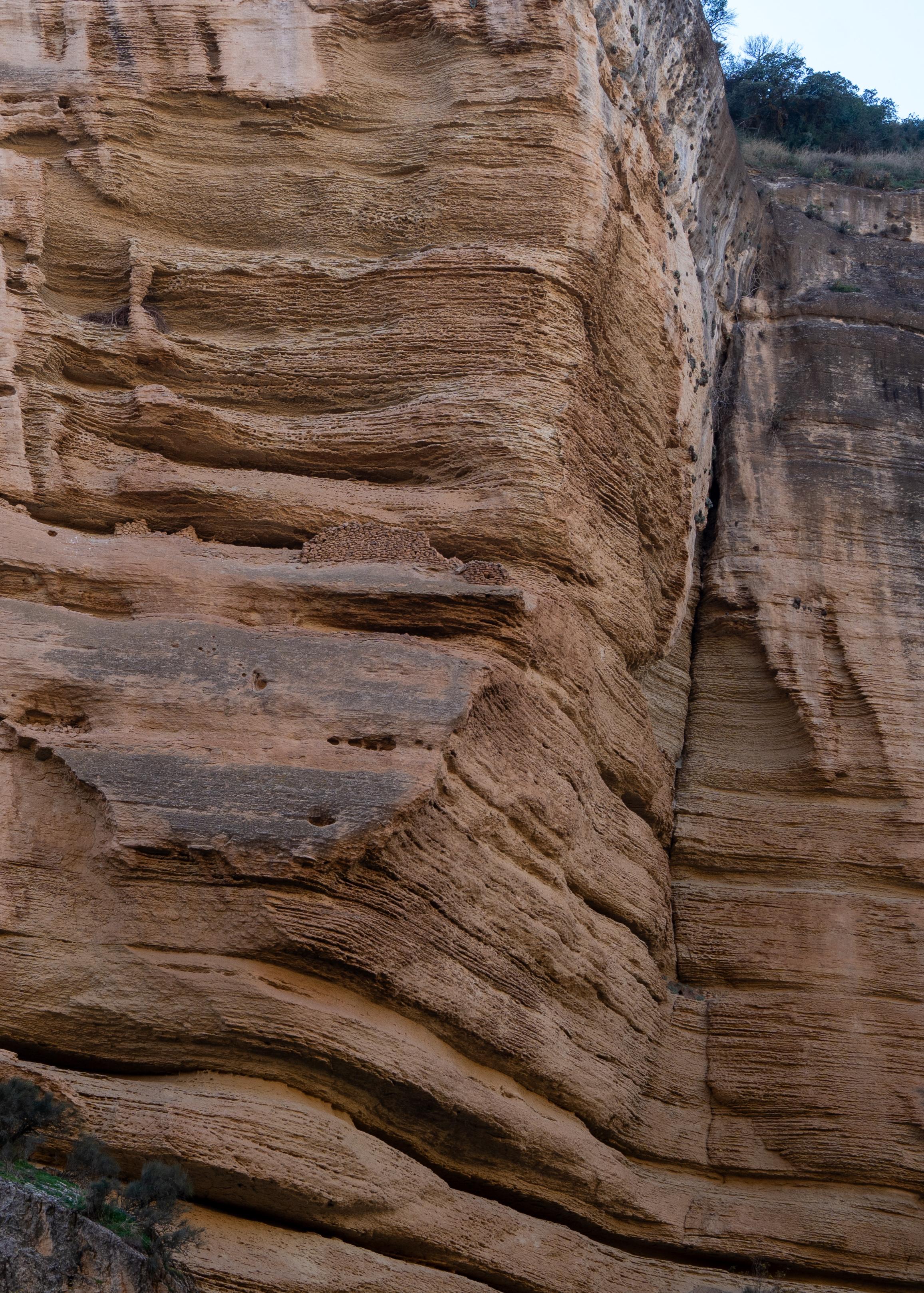 An orange cliff face with horizontal ledges. One of the ledges has a wall built of stones