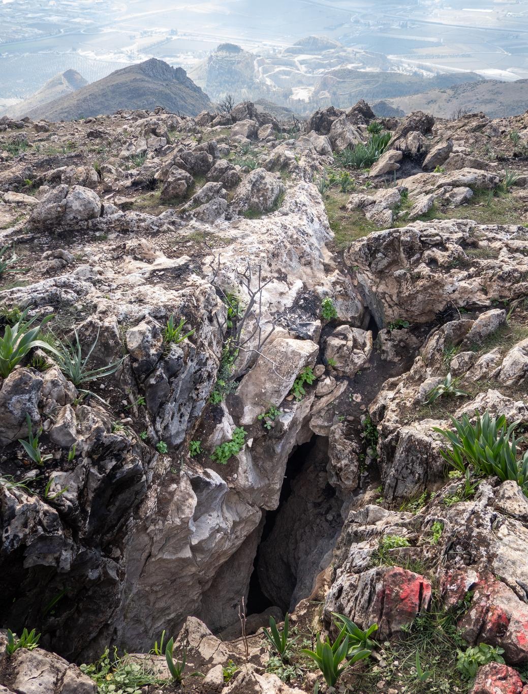 A large crack in the mountain top shows a deep 160m deep hole. Small green plants are growing round the side of the hole